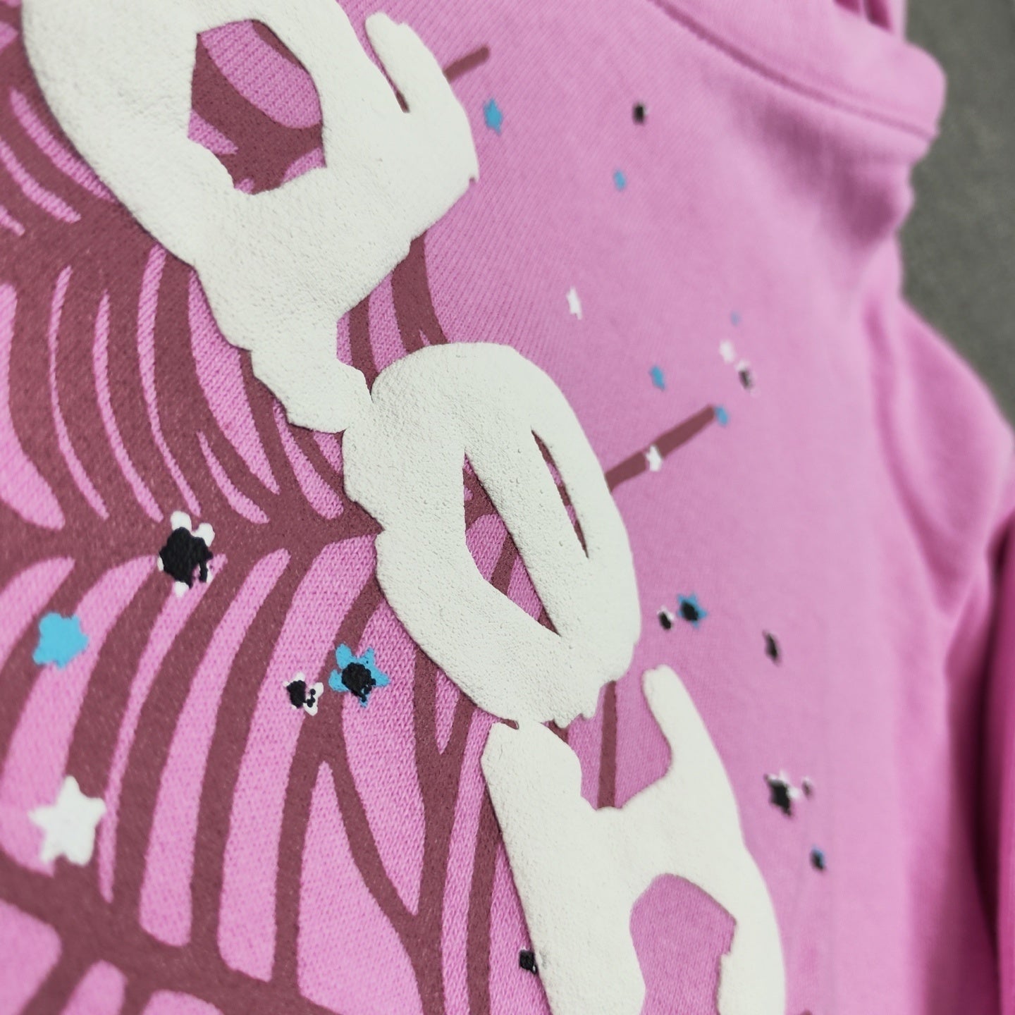 Full puff-print artwork on Sp5der OG Web Hoodie Pink with white logo, spider web and scattered stars
Close-up of raised white Sp5der lettering and star print details on the pink OG Web Hoodie
Side angle showing the raised three-dimensional puff-print texture on Sp5der OG Web Hoodie Pink