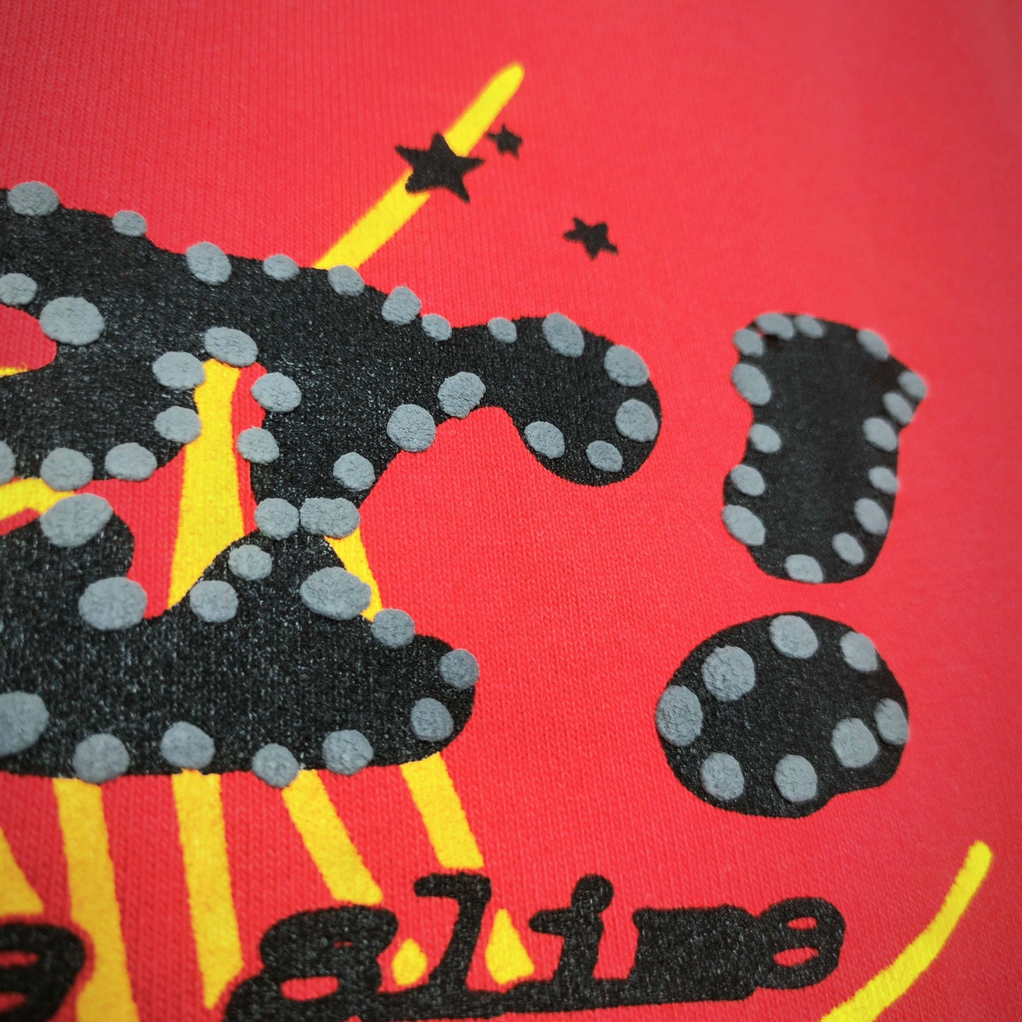 Full front artwork on Sp5der P*NK V2 Hoodie Red with black puff logo, yellow web and stars
Close-up of raised black SP5DER puff-print lettering with dotted details on the red hoodie
Side angle showing the three-dimensional black puff-print texture on Sp5der P*NK V2 Hoodie Red
Close-up of yellow spider-web artwork and black star details on Sp5der P*NK V2 Hoodie Red