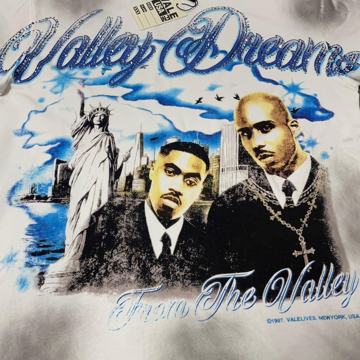 Vale Forever Godfather Bling Tee distressed portrait print close-up
Vale Forever Godfather Bling Tee blue jeweled Valley Dreams lettering
Vale Forever Godfather Bling Tee sparkling crystal lettering detail
Vale Forever Godfather Bling Tee distressed dual portrait graphic detail
Vale Forever Godfather Bling Tee New York skyline print detail
Vale Forever Godfather Bling Tee blue sky and flying birds graphic detail
Vale Forever Godfather Bling Tee From The Valley script print detail