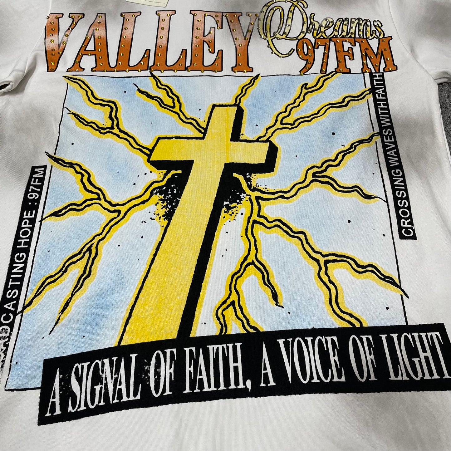 Vale Forever Thunder Cross Bling Tee full cross and lightning front graphic
Vale Forever Thunder Cross Bling Tee oversized yellow cross graphic
Vale Forever Thunder Cross Bling Tee distressed graphic print close-up
Vale Forever Thunder Cross Bling Tee crystal Valley lettering detail
Vale Forever Thunder Cross Bling Tee Dreams 97FM lettering detail
Vale Forever Thunder Cross Bling Tee sparkling crystal embellishment close-up
Vale Forever Thunder Cross Bling Tee yellow cross print detail
