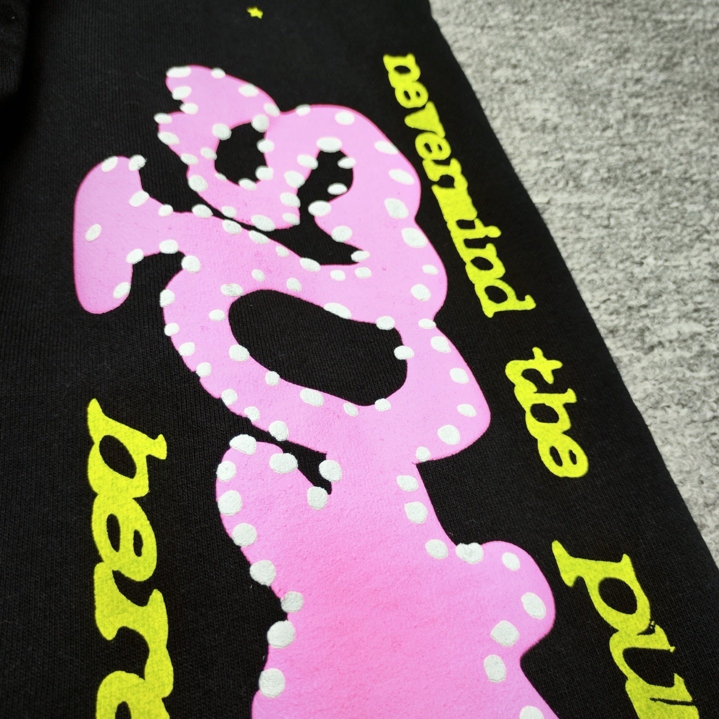 Close-up of pink P*NK rhinestone leg graphic on black Sp5der sweatpants