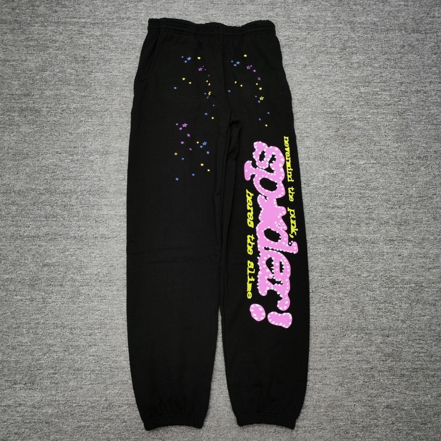 Sp5der P*NK sweatpants black front view with pink rhinestone logo and multicolor star graphics