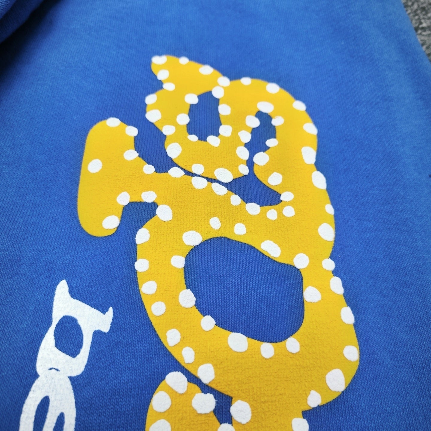 Yellow puff-print SP5DER graphic on TC Blue sweatpants
Close-up of yellow SP5DER puff-print graphic on blue sweatpants