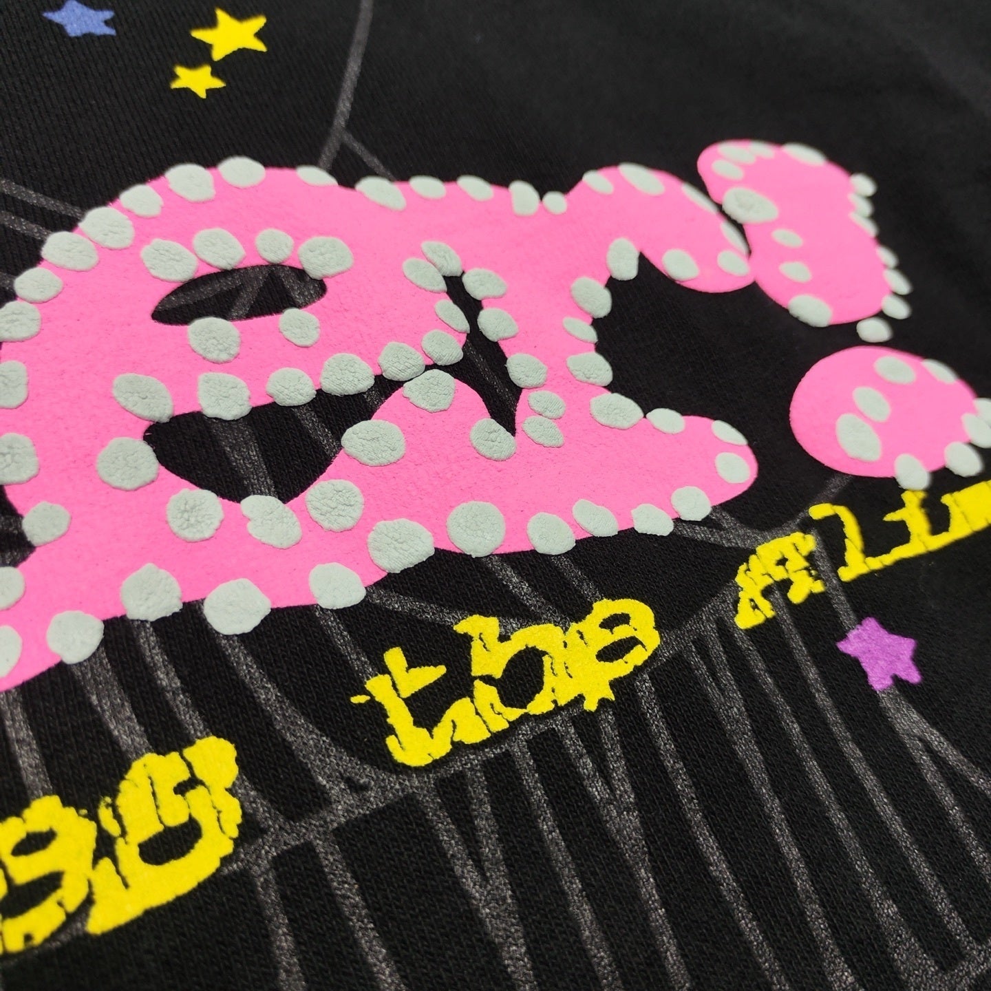 Close-up of raised puff print, pink P*NK lettering and spider web graphic on Sp5der black hoodie