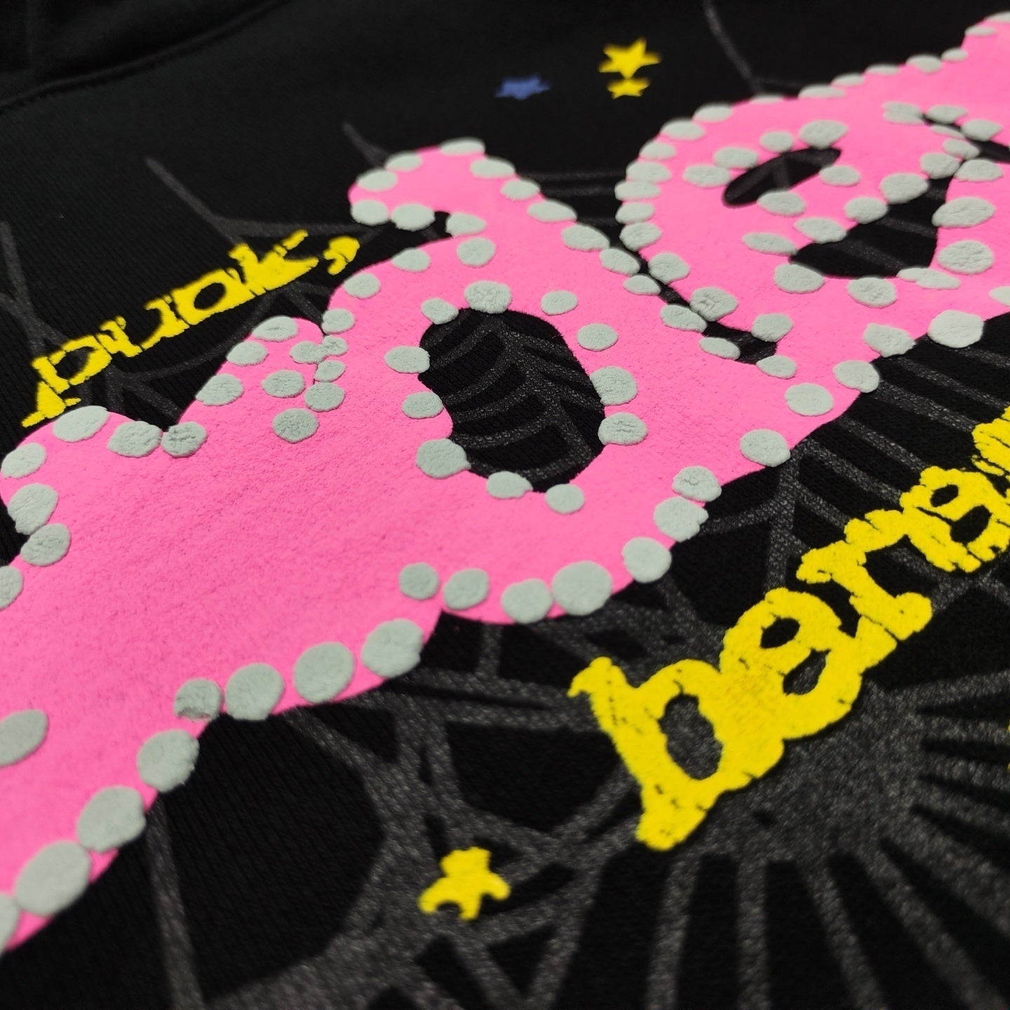 Close-up of raised puff print, pink P*NK lettering and spider web graphic on Sp5der black hoodie