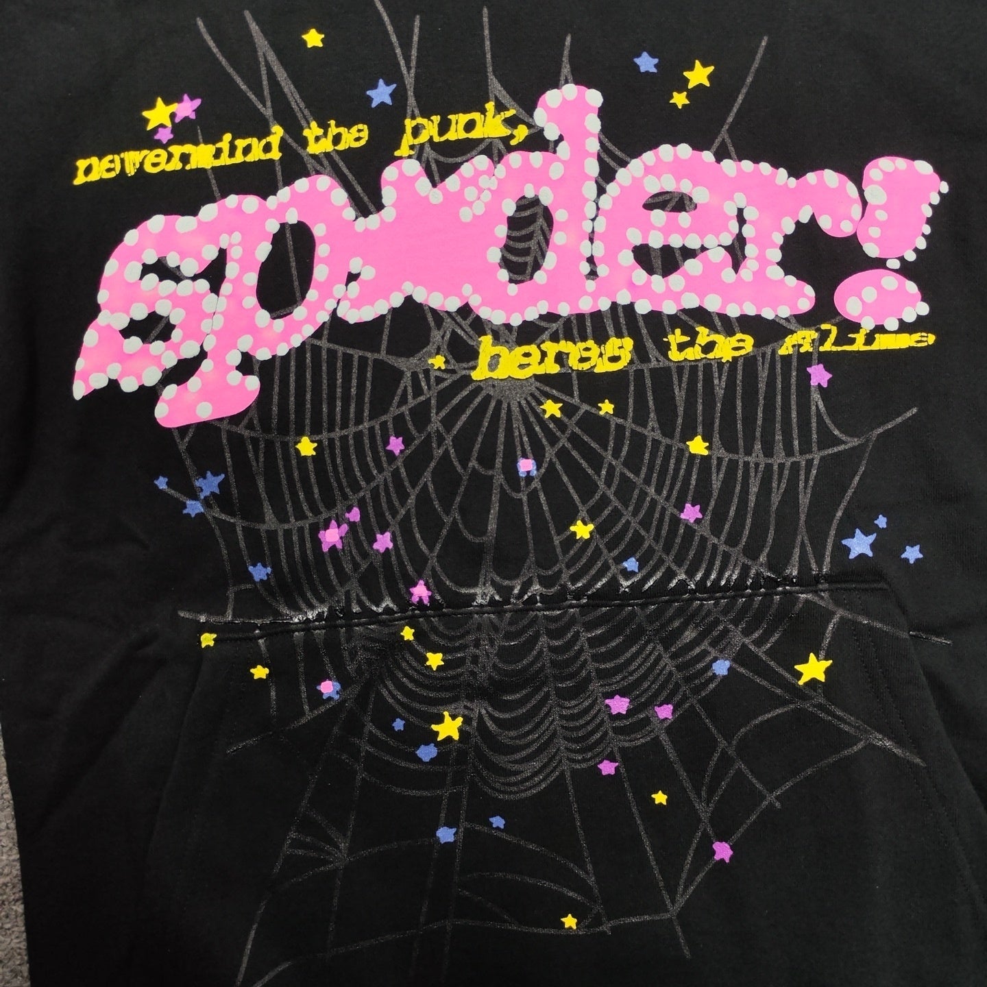 Close-up of raised puff print, pink P*NK lettering and spider web graphic on Sp5der black hoodie