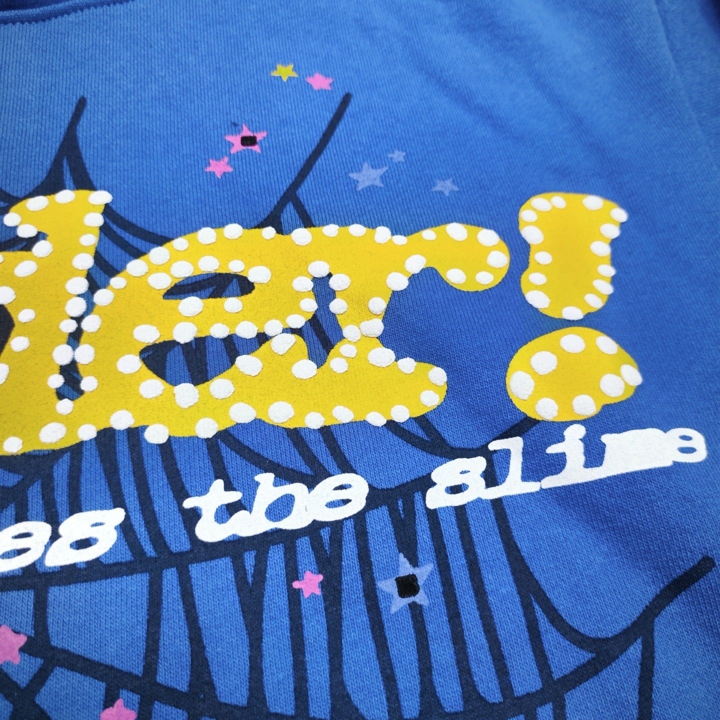 Full puff print artwork on Sp5der TC Blue Hoodie with yellow lettering, black spider web and colorful stars
Close-up of yellow raised puff lettering on Sp5der TC Blue Here's the Slime Hoodie
Side angle showing the three-dimensional raised puff print texture on Sp5der TC Blue Hoodie