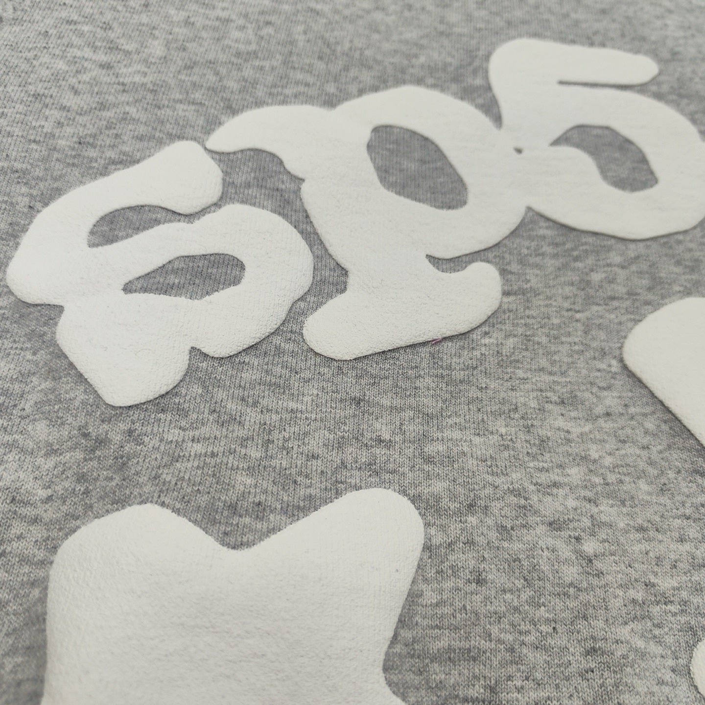 Full white puff-print artwork on Sp5der Beluga Hoodie Heather Grey with oversized logo and stars
Close-up of white puff-print lettering and star graphics on Sp5der Beluga Hoodie Heather Grey
Side angle showing the raised three-dimensional puff-print texture on Sp5der Beluga Hoodie