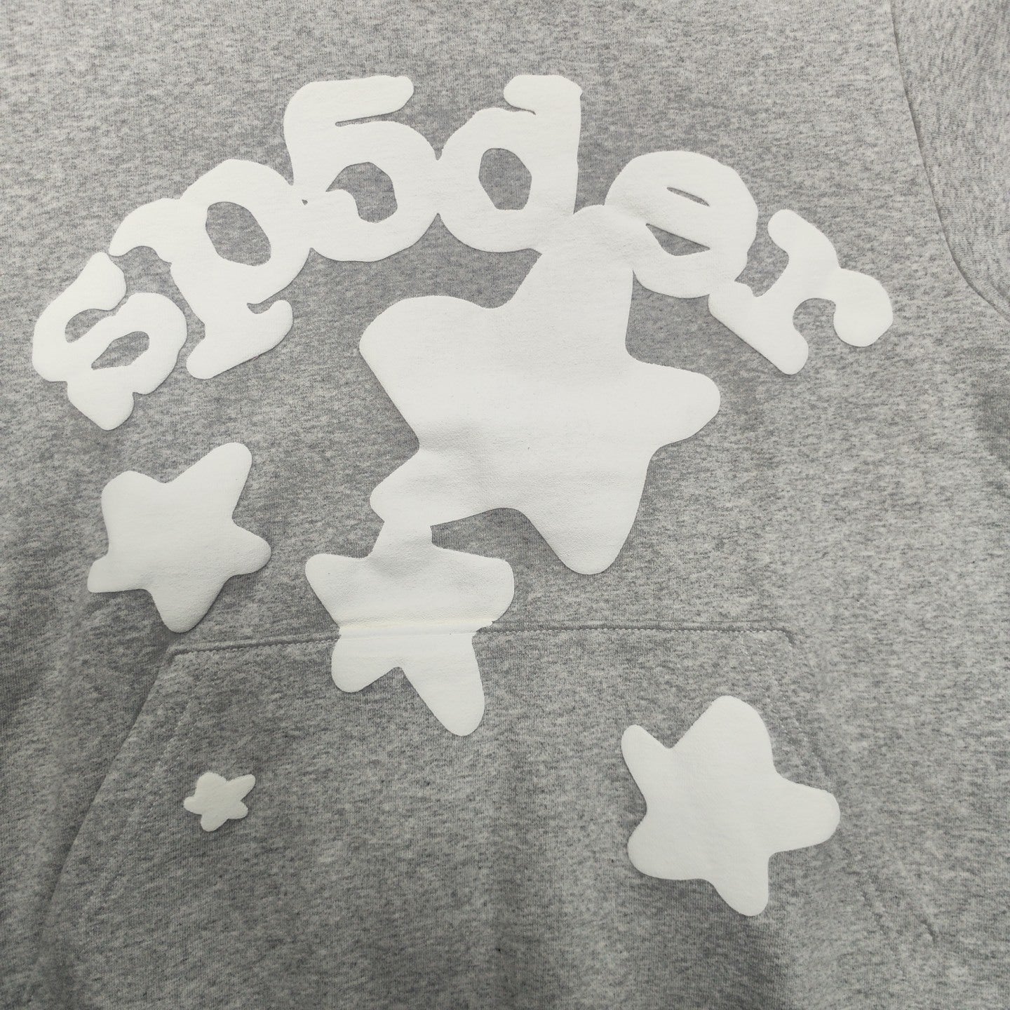 Full white puff-print artwork on Sp5der Beluga Hoodie Heather Grey with oversized logo and stars
Close-up of white puff-print lettering and star graphics on Sp5der Beluga Hoodie Heather Grey
Side angle showing the raised three-dimensional puff-print texture on Sp5der Beluga Hoodie