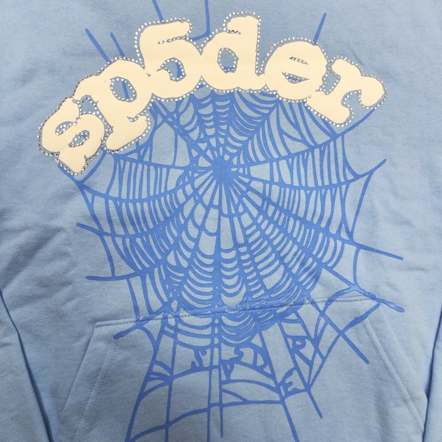 Full puff-print artwork on Sp5der Web Hoodie Sky Blue with white logo and signature blue spider web
Close-up of white puff-print Sp5der lettering and rhinestone edge details on Sky Blue Hoodie
Side angle showing the raised three-dimensional puff logo and rhinestone trim on Sp5der Sky Blue Hoodie