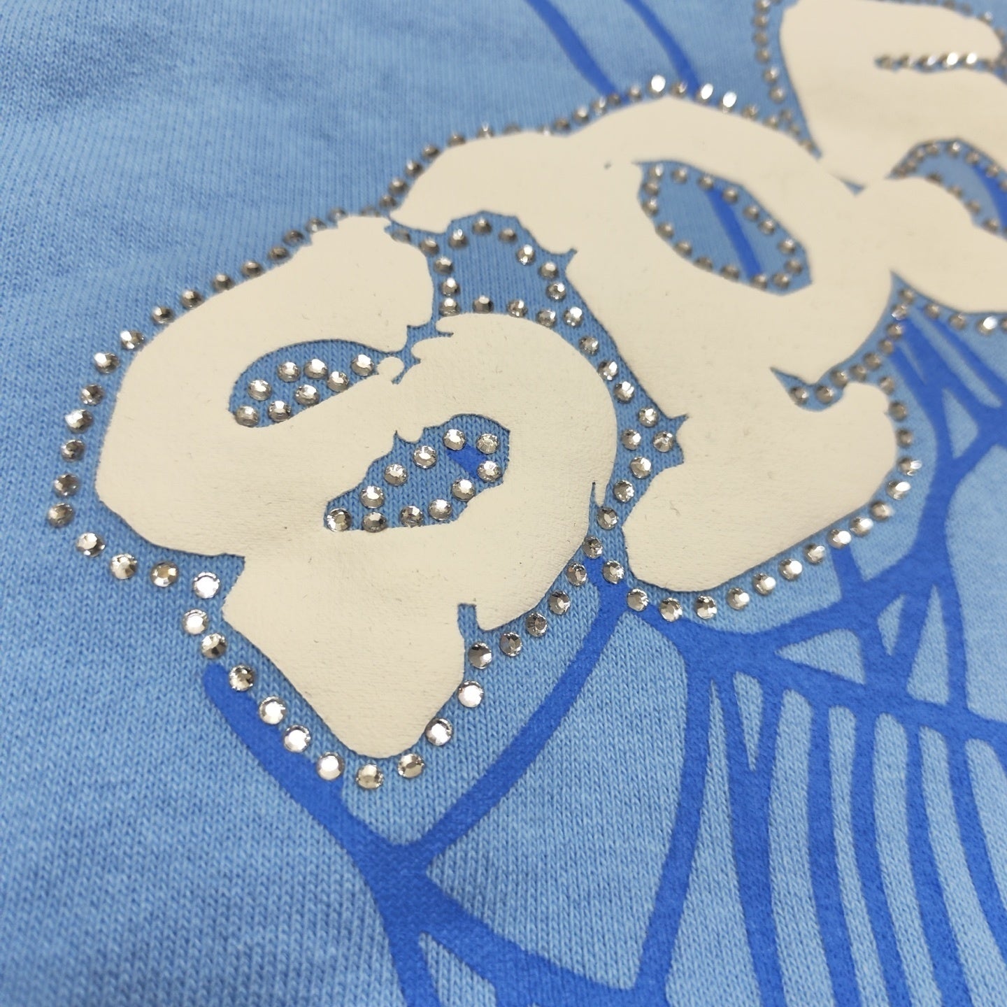 Full puff-print artwork on Sp5der Web Hoodie Sky Blue with white logo and signature blue spider web
Close-up of white puff-print Sp5der lettering and rhinestone edge details on Sky Blue Hoodie
Side angle showing the raised three-dimensional puff logo and rhinestone trim on Sp5der Sky Blue Hoodie