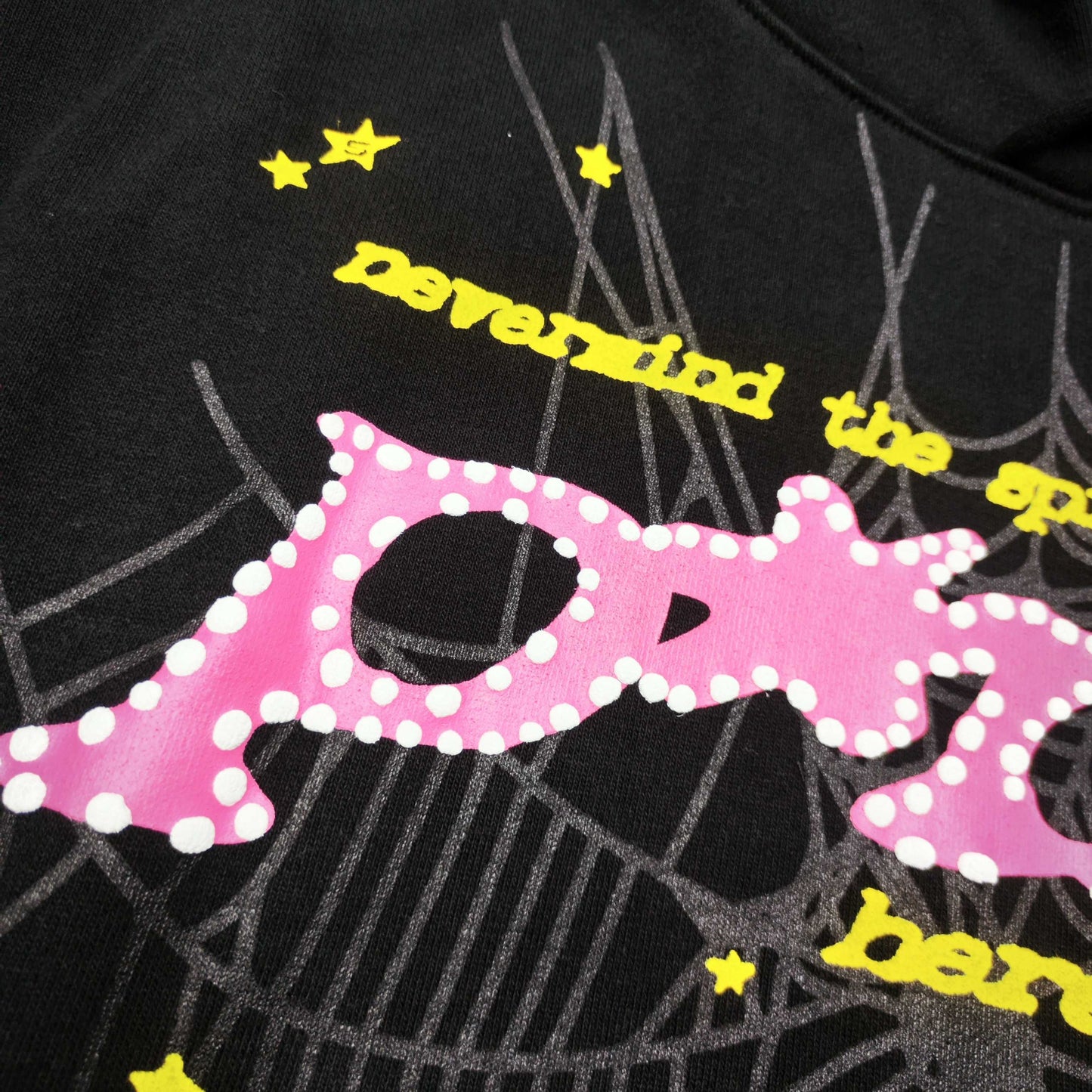 Full graphic artwork on Sp5der P*NK Hoodie Black with pink puff lettering, web print and colorful stars
Close-up of raised pink P*NK lettering and white dot details on Sp5der Black Hoodie
Side angle showing the three-dimensional pink puff-print texture on Sp5der P*NK Hoodie Black