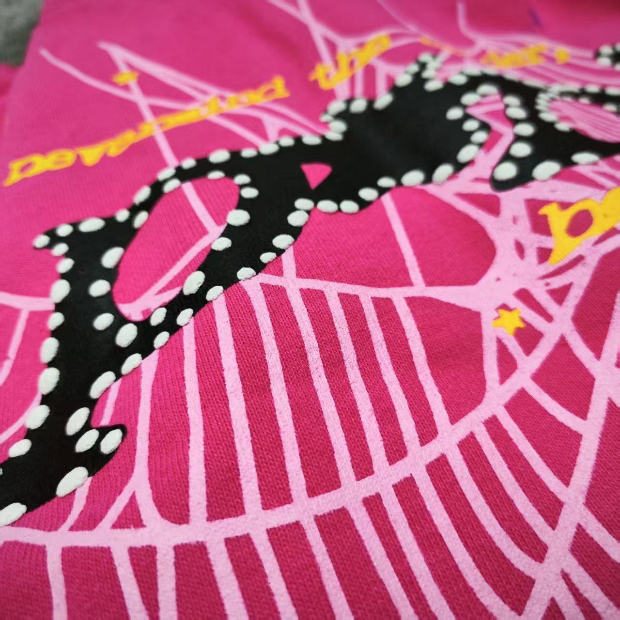 Full graphic artwork on Sp5der P*NK Hoodie Pink with black logo, white web and colorful stars
Close-up of black P*NK lettering with white dot trim on Sp5der Pink Hoodie
Side angle showing the raised three-dimensional graphic texture on Sp5der P*NK Hoodie Pink