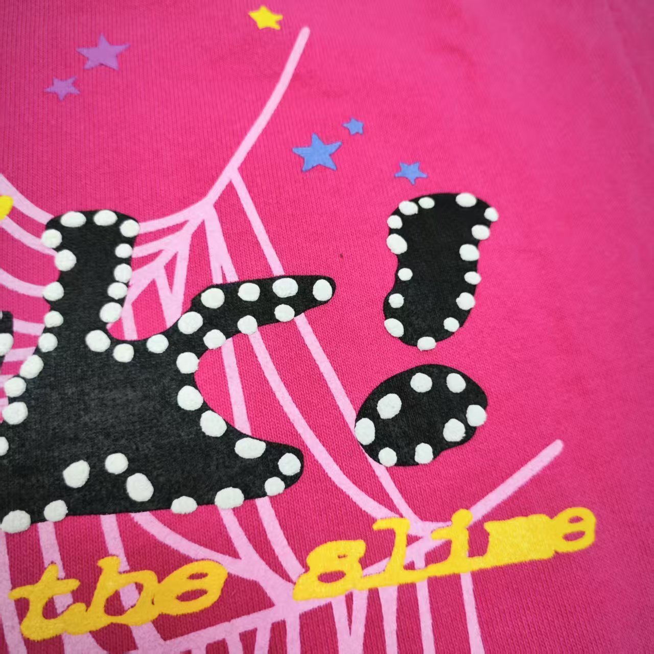 Full graphic artwork on Sp5der P*NK Hoodie Pink with black logo, white web and colorful stars
Close-up of black P*NK lettering with white dot trim on Sp5der Pink Hoodie
Side angle showing the raised three-dimensional graphic texture on Sp5der P*NK Hoodie Pink