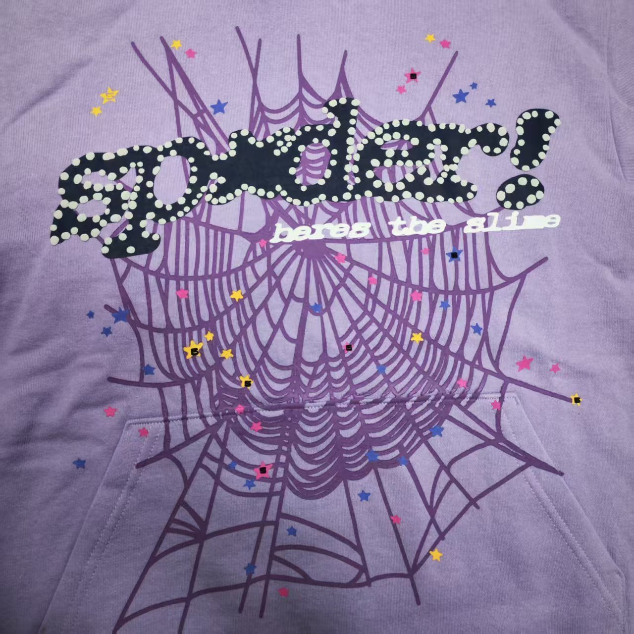 Full puff-print artwork on Sp5der Acai Hoodie Purple with black logo, tonal web and colorful stars
Close-up of raised black Sp5der lettering with dotted trim on Acai Purple Hoodie
Side angle showing the three-dimensional puff-print texture on Sp5der Acai Hoodie Purple