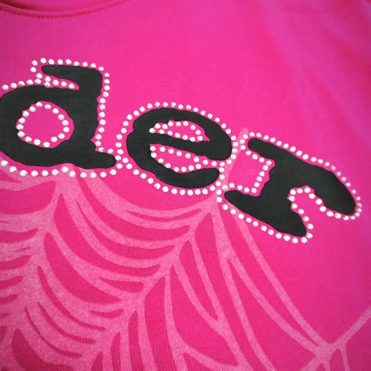 Full front artwork on Sp5der Legacy Hoodie Pink White with puff lettering, rhinestones and spider web
Close-up of raised black SP5DER puff-print lettering on the pink Legacy Hoodie
Close-up of rhinestone trim surrounding the black SP5DER lettering on the pink Legacy Hoodie
Side angle showing raised puff lettering and three-dimensional rhinestone details on Sp5der Legacy Hoodie