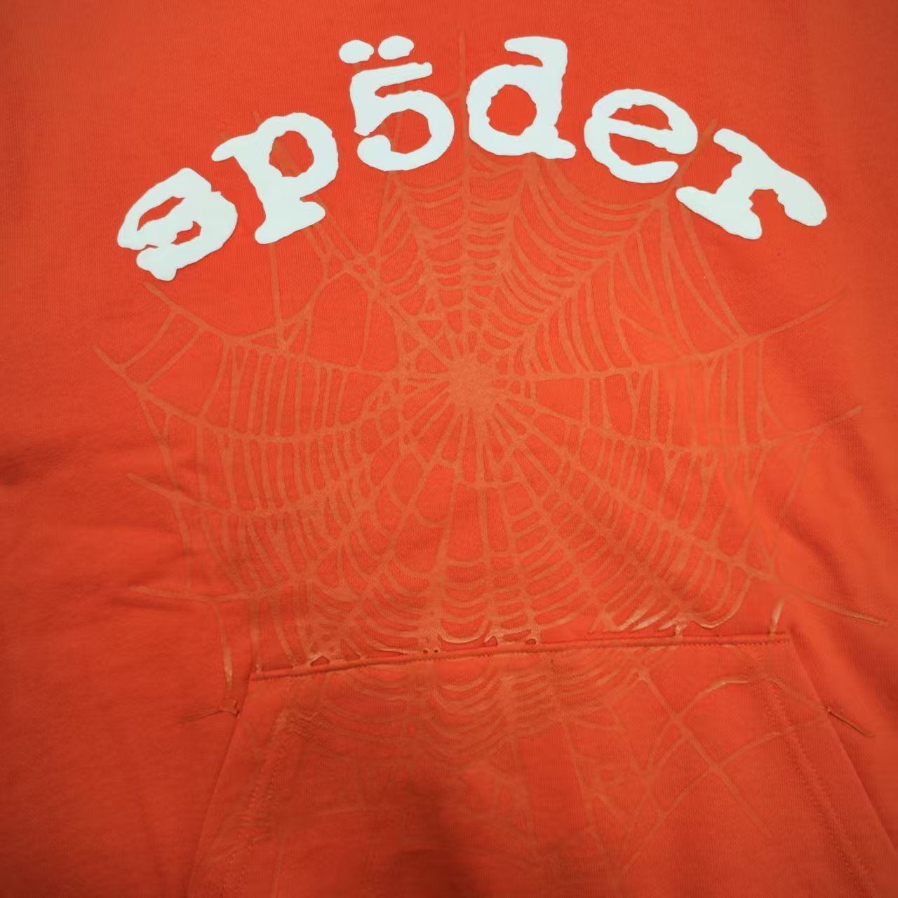 Full front artwork on Sp5der Orange Hoodie with raised white logo and tonal spider-web graphic
Close-up of raised white Sp5der lettering on the Orange Logo Hoodie Sweatshirt
Side angle showing the raised three-dimensional white logo detail on Sp5der Orange Hoodie
Close-up of tonal spider-web artwork printed across the front of Sp5der Orange Hoodie