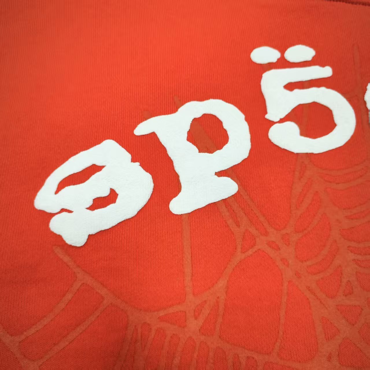 Full front artwork on Sp5der Orange Hoodie with raised white logo and tonal spider-web graphic
Close-up of raised white Sp5der lettering on the Orange Logo Hoodie Sweatshirt
Side angle showing the raised three-dimensional white logo detail on Sp5der Orange Hoodie
Close-up of tonal spider-web artwork printed across the front of Sp5der Orange Hoodie
