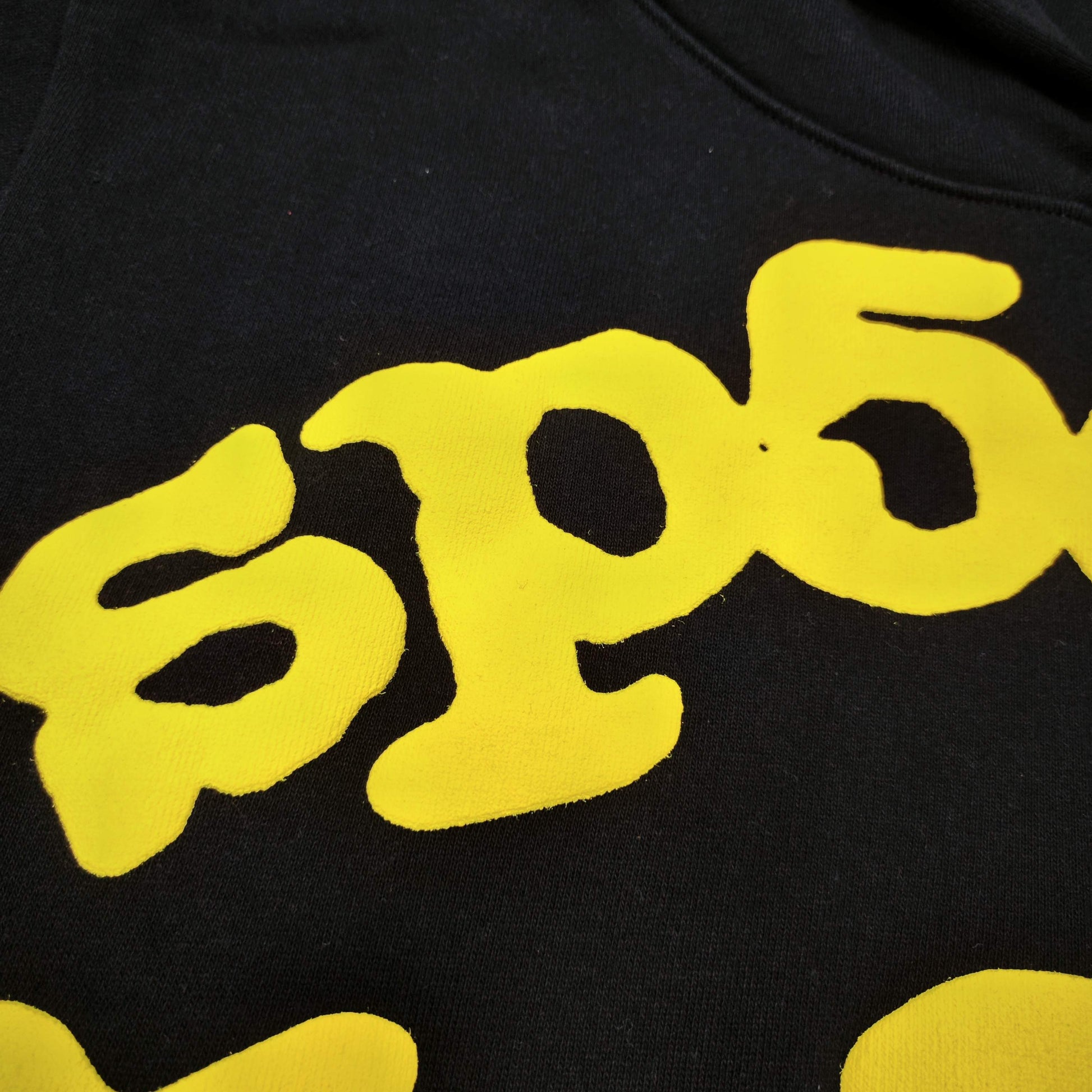 Full yellow puff-print artwork on Sp5der Beluga Hoodie Onyx Yellow with logo and star graphics
Close-up of raised yellow Sp5der lettering and smooth puff-print edges on the black Beluga Hoodie
Side angle showing the three-dimensional yellow puff-print texture on Sp5der Beluga Hoodie
Yellow star and number graphics printed across the sleeve of Sp5der Beluga Hoodie Onyx Yellow