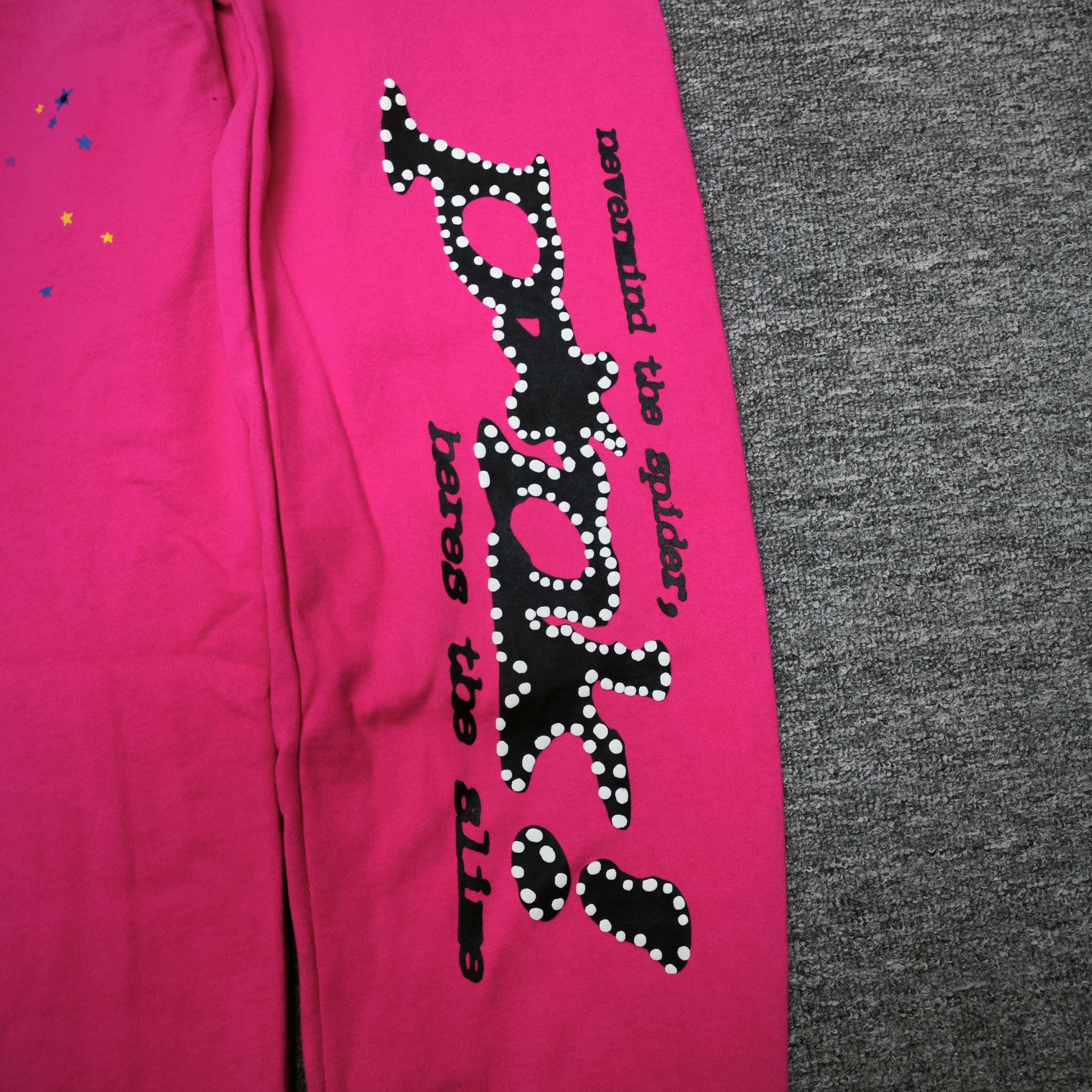 Black SP5DER leg graphic and multicolor star prints on pink P*NK V2 sweatpants