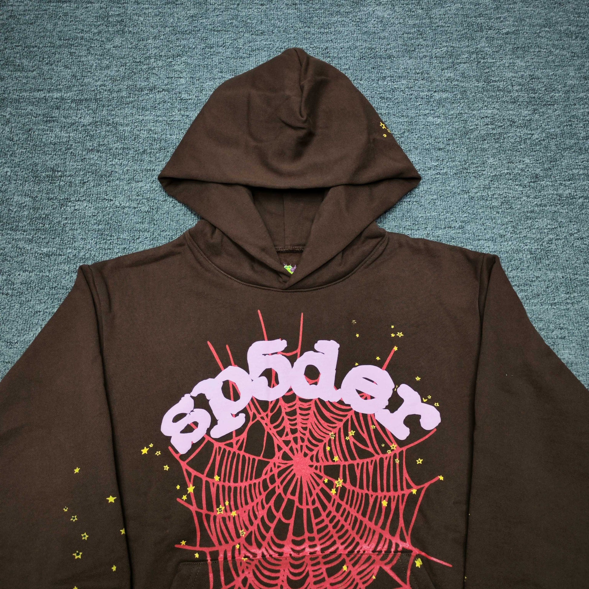 Full front artwork on Sp5der Web Hoodie Brown with pink puff logo, red web and yellow stars
Close-up of raised pink Sp5der puff-print lettering on the Brown Web Hoodie
Side angle showing the three-dimensional pink puff-print texture on Sp5der Web Hoodie Brown
Close-up of red spider-web artwork and yellow star details on Sp5der Web Hoodie Brown