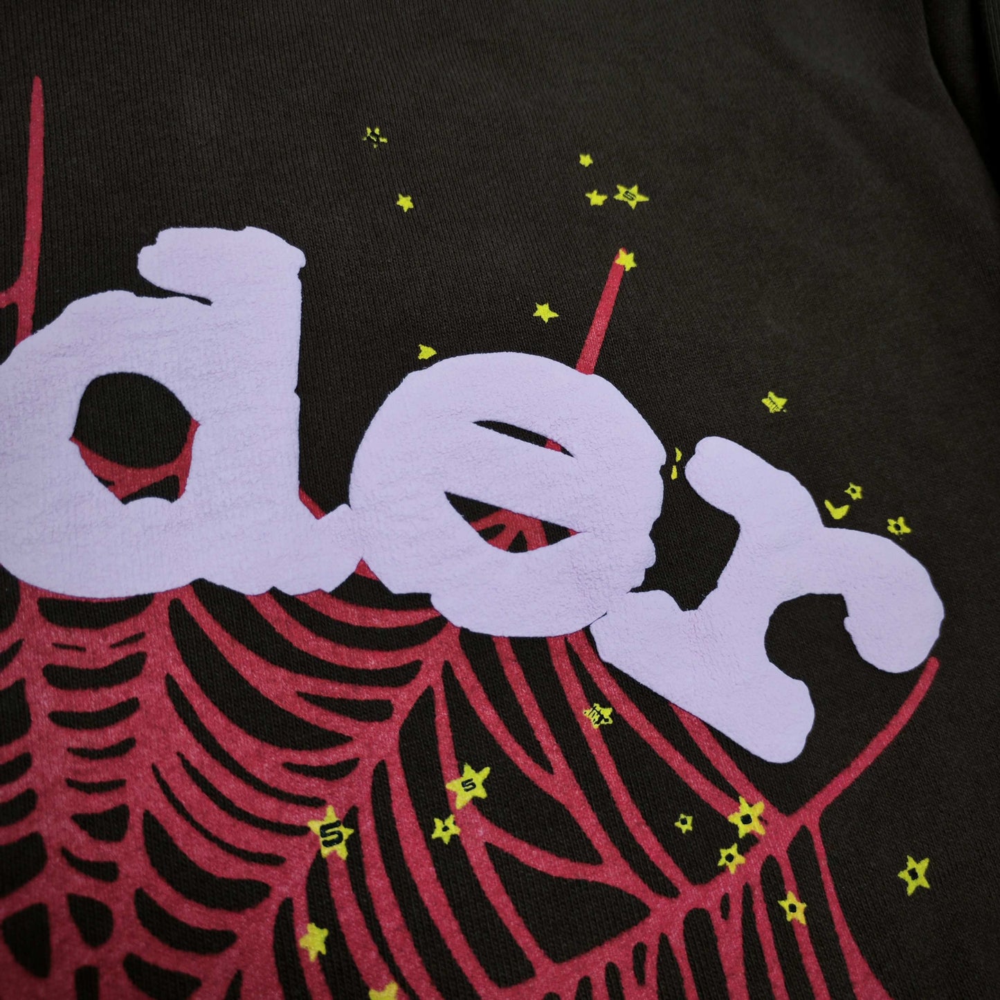 Full front artwork on Sp5der Web Hoodie Brown with pink puff logo, red web and yellow stars
Close-up of raised pink Sp5der puff-print lettering on the Brown Web Hoodie
Side angle showing the three-dimensional pink puff-print texture on Sp5der Web Hoodie Brown
Close-up of red spider-web artwork and yellow star details on Sp5der Web Hoodie Brown