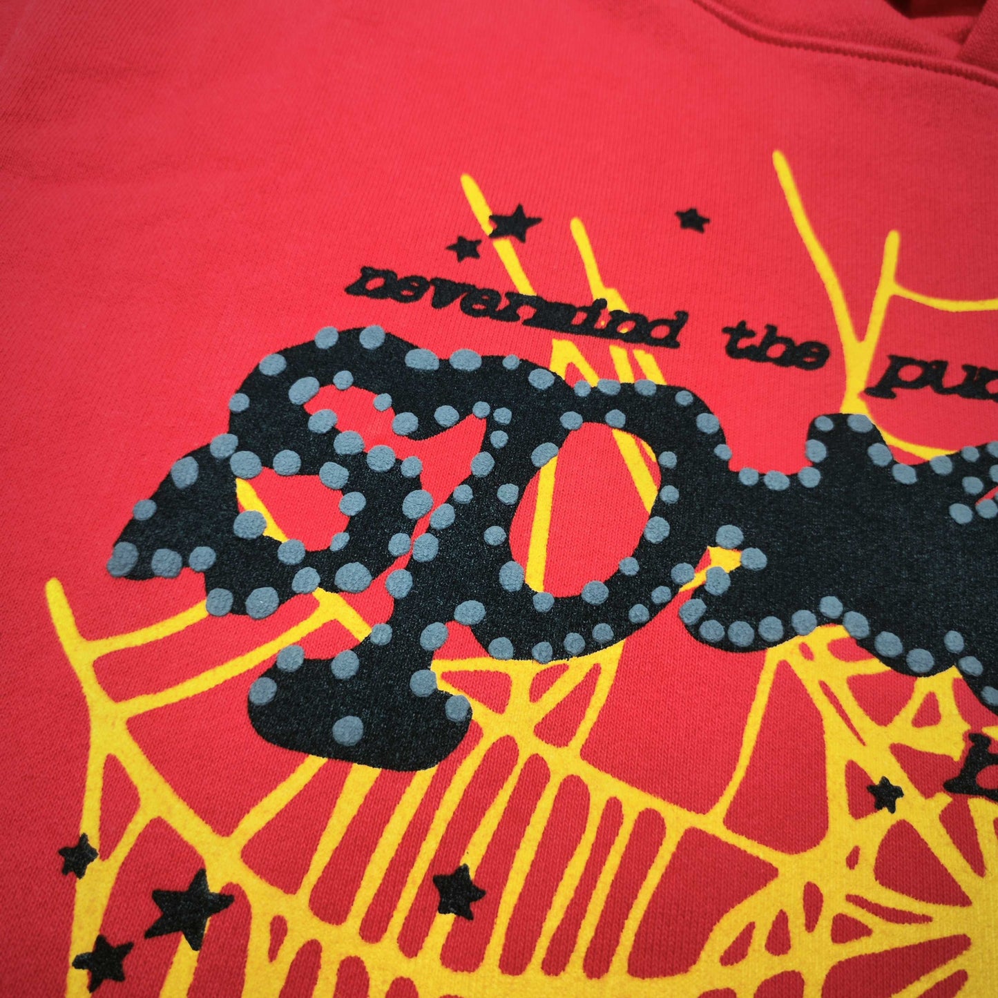 Full front artwork on Sp5der P*NK V2 Hoodie Red with black puff logo, yellow web and stars
Close-up of raised black SP5DER puff-print lettering with dotted details on the red hoodie
Side angle showing the three-dimensional black puff-print texture on Sp5der P*NK V2 Hoodie Red
Close-up of yellow spider-web artwork and black star details on Sp5der P*NK V2 Hoodie Red