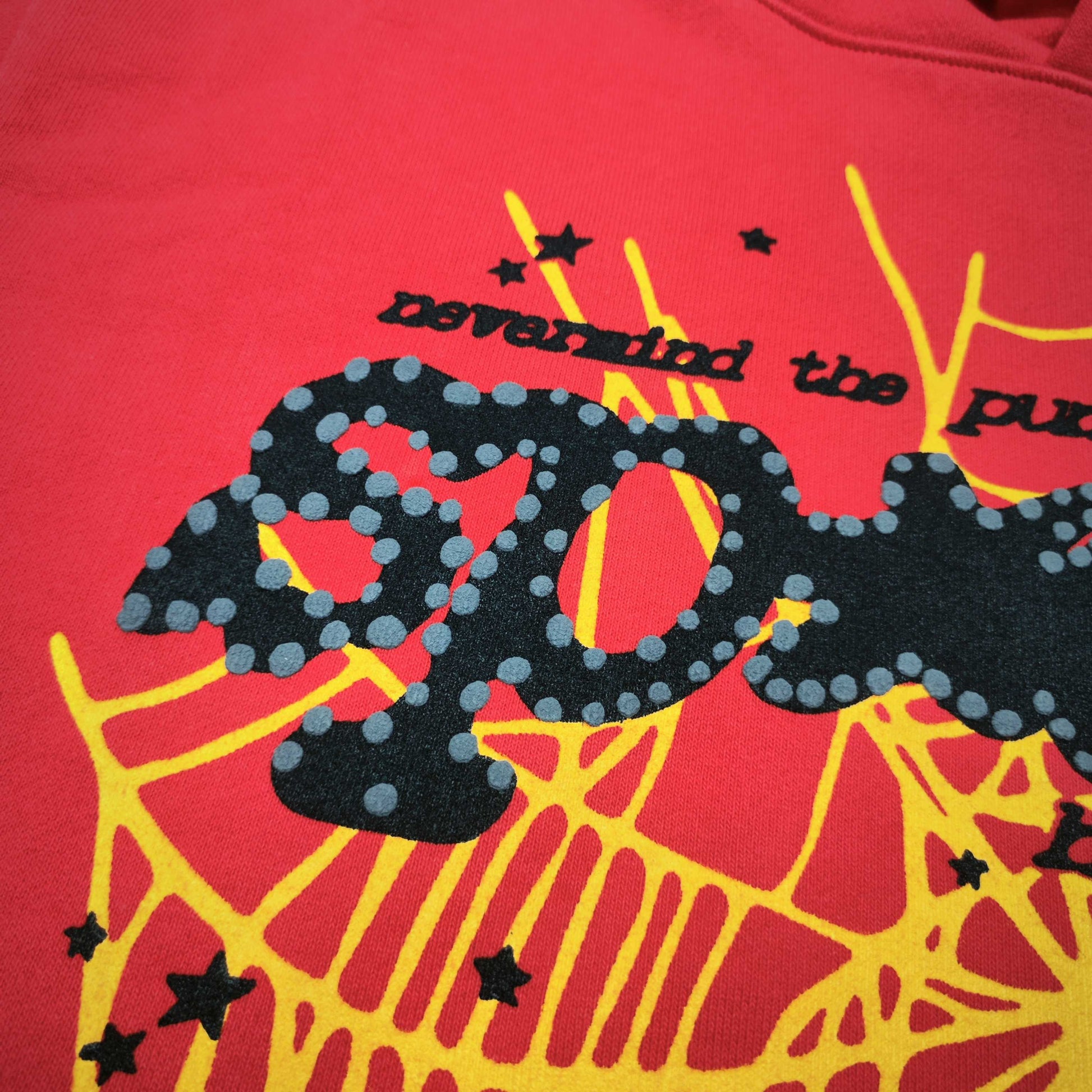 Full front artwork on Sp5der P*NK V2 Hoodie Red with black puff logo, yellow web and stars
Close-up of raised black SP5DER puff-print lettering with dotted details on the red hoodie
Side angle showing the three-dimensional black puff-print texture on Sp5der P*NK V2 Hoodie Red
Close-up of yellow spider-web artwork and black star details on Sp5der P*NK V2 Hoodie Red