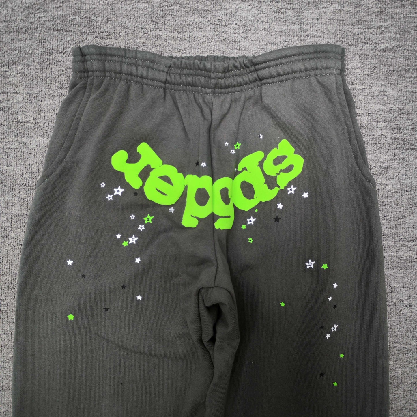 Neon green SP5DER logo and scattered star graphics on slate grey Wait Web sweatpants