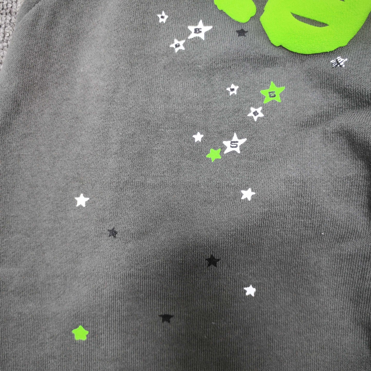 Scattered black white and green star graphics on SP5DER Wait Web sweatpants