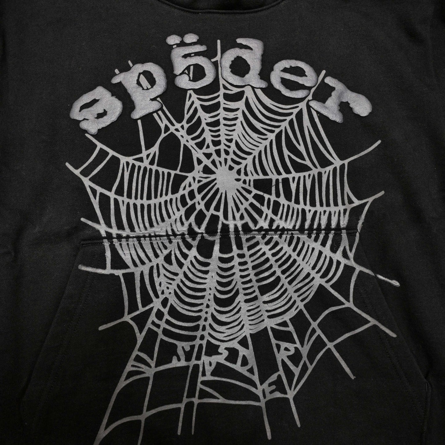 Full front artwork on Sp5der OG Web Hoodie Black with raised grey logo and tonal spider web
Close-up of raised dark-grey SP5DER lettering on the black OG Web Hoodie
Side angle showing the three-dimensional raised logo texture on Sp5der OG Web Hoodie Black
Close-up of tonal dark-grey spider-web artwork on Sp5der OG Web Hoodie Black
Close-up of tonal web graphic alignment around the kangaroo pocket on Sp5der black hoodie