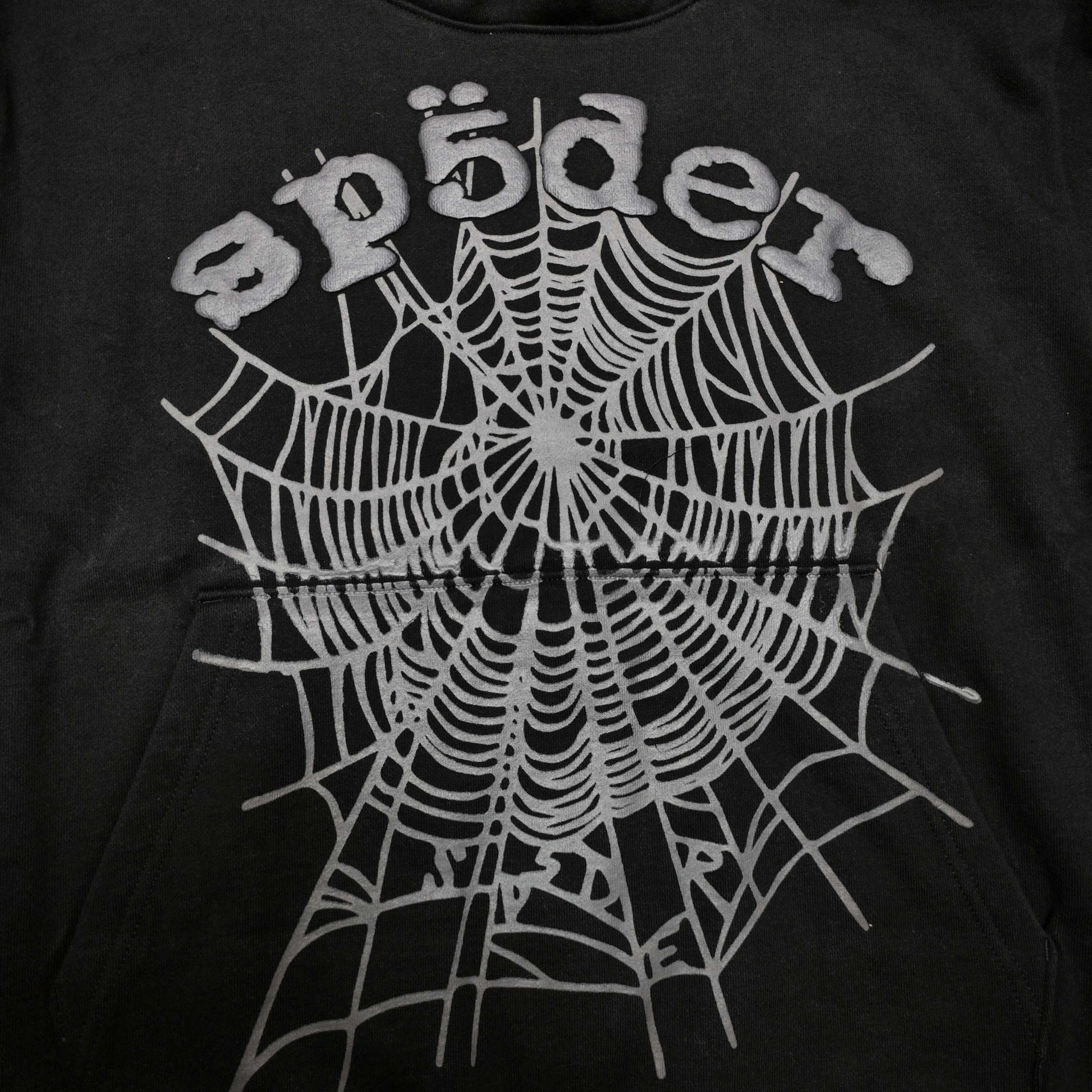 Full front artwork on Sp5der OG Web Hoodie Black with raised grey logo and tonal spider web
Close-up of raised dark-grey SP5DER lettering on the black OG Web Hoodie
Side angle showing the three-dimensional raised logo texture on Sp5der OG Web Hoodie Black
Close-up of tonal dark-grey spider-web artwork on Sp5der OG Web Hoodie Black
Close-up of tonal web graphic alignment around the kangaroo pocket on Sp5der black hoodie