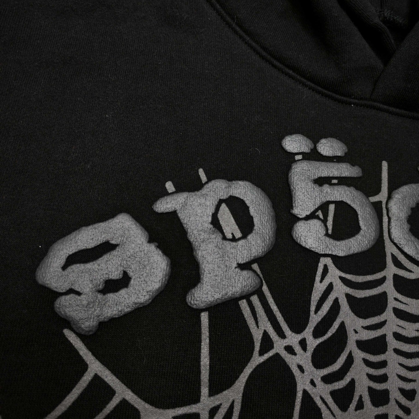 Full front artwork on Sp5der OG Web Hoodie Black with raised grey logo and tonal spider web
Close-up of raised dark-grey SP5DER lettering on the black OG Web Hoodie
Side angle showing the three-dimensional raised logo texture on Sp5der OG Web Hoodie Black
Close-up of tonal dark-grey spider-web artwork on Sp5der OG Web Hoodie Black
Close-up of tonal web graphic alignment around the kangaroo pocket on Sp5der black hoodie