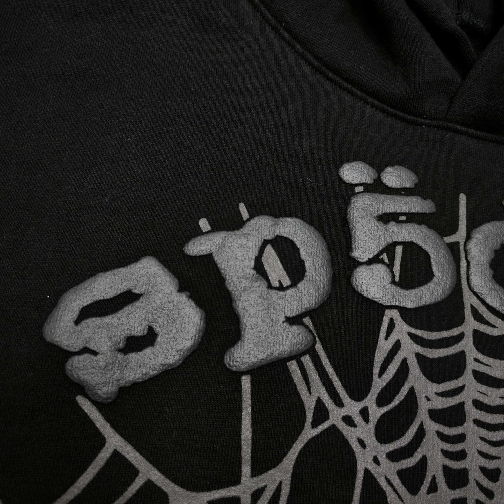 Full front artwork on Sp5der OG Web Hoodie Black with raised grey logo and tonal spider web
Close-up of raised dark-grey SP5DER lettering on the black OG Web Hoodie
Side angle showing the three-dimensional raised logo texture on Sp5der OG Web Hoodie Black
Close-up of tonal dark-grey spider-web artwork on Sp5der OG Web Hoodie Black
Close-up of tonal web graphic alignment around the kangaroo pocket on Sp5der black hoodie