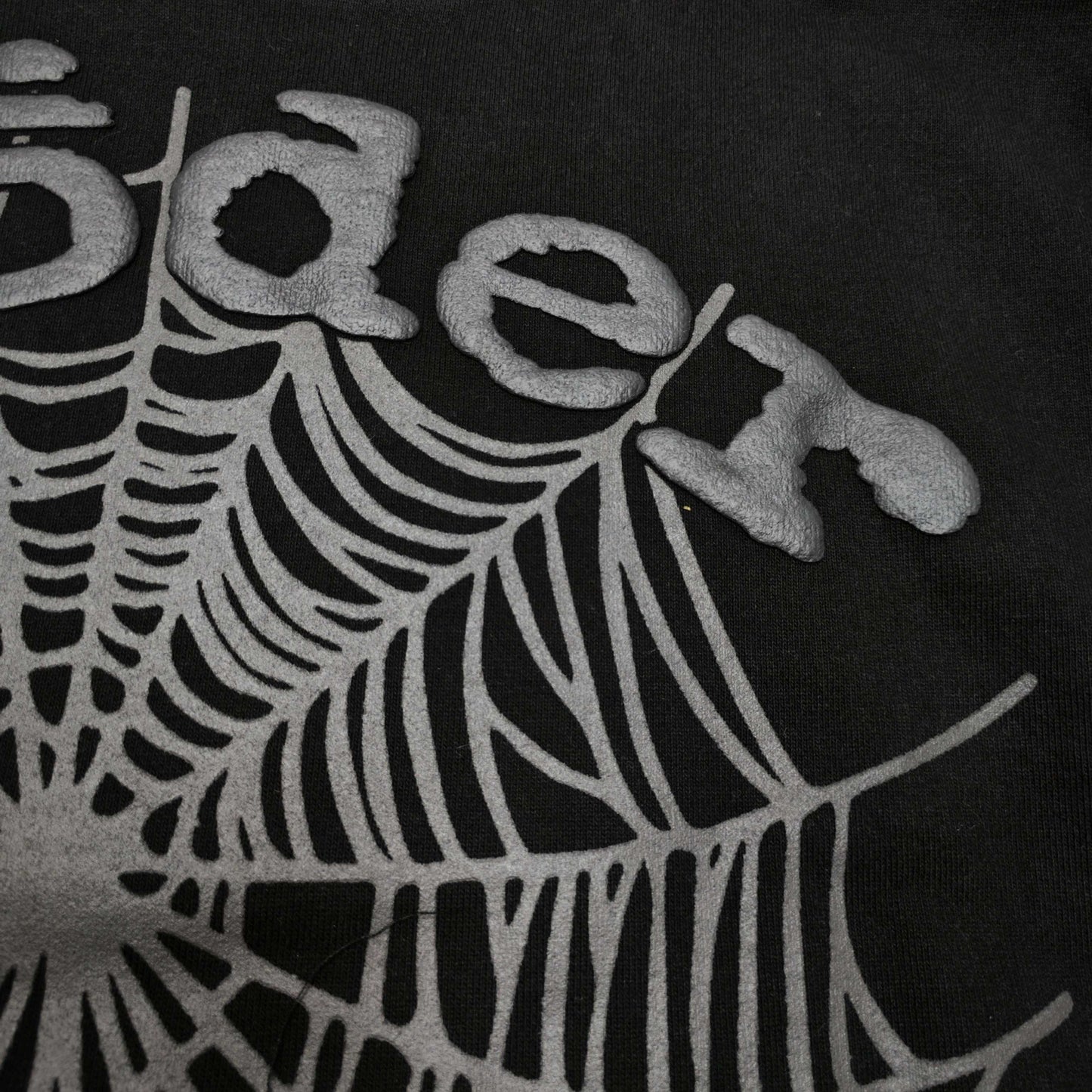 Full front artwork on Sp5der OG Web Hoodie Black with raised grey logo and tonal spider web
Close-up of raised dark-grey SP5DER lettering on the black OG Web Hoodie
Side angle showing the three-dimensional raised logo texture on Sp5der OG Web Hoodie Black
Close-up of tonal dark-grey spider-web artwork on Sp5der OG Web Hoodie Black
Close-up of tonal web graphic alignment around the kangaroo pocket on Sp5der black hoodie