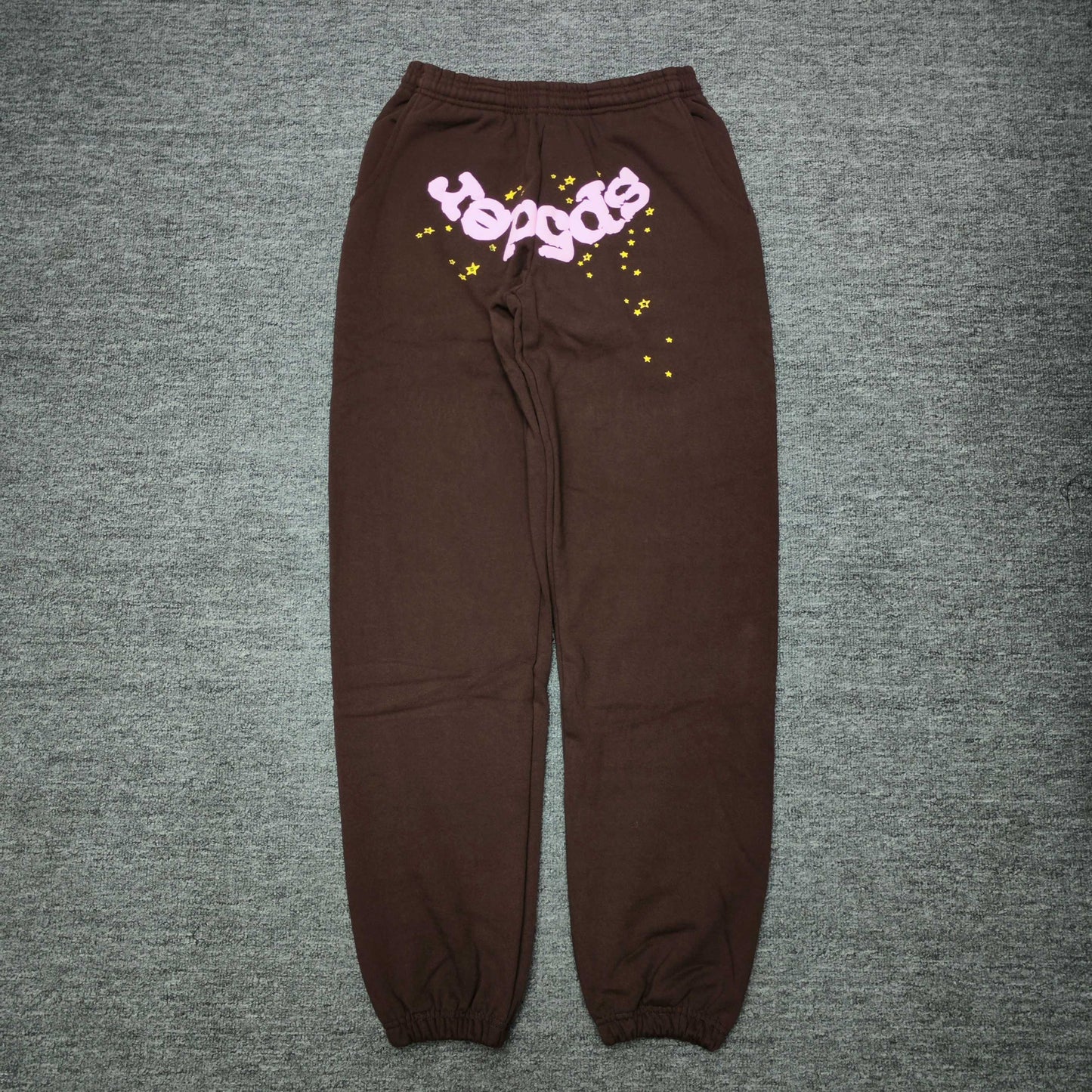 SP5DER Classic brown sweatpants front view with pink logo and yellow star graphics