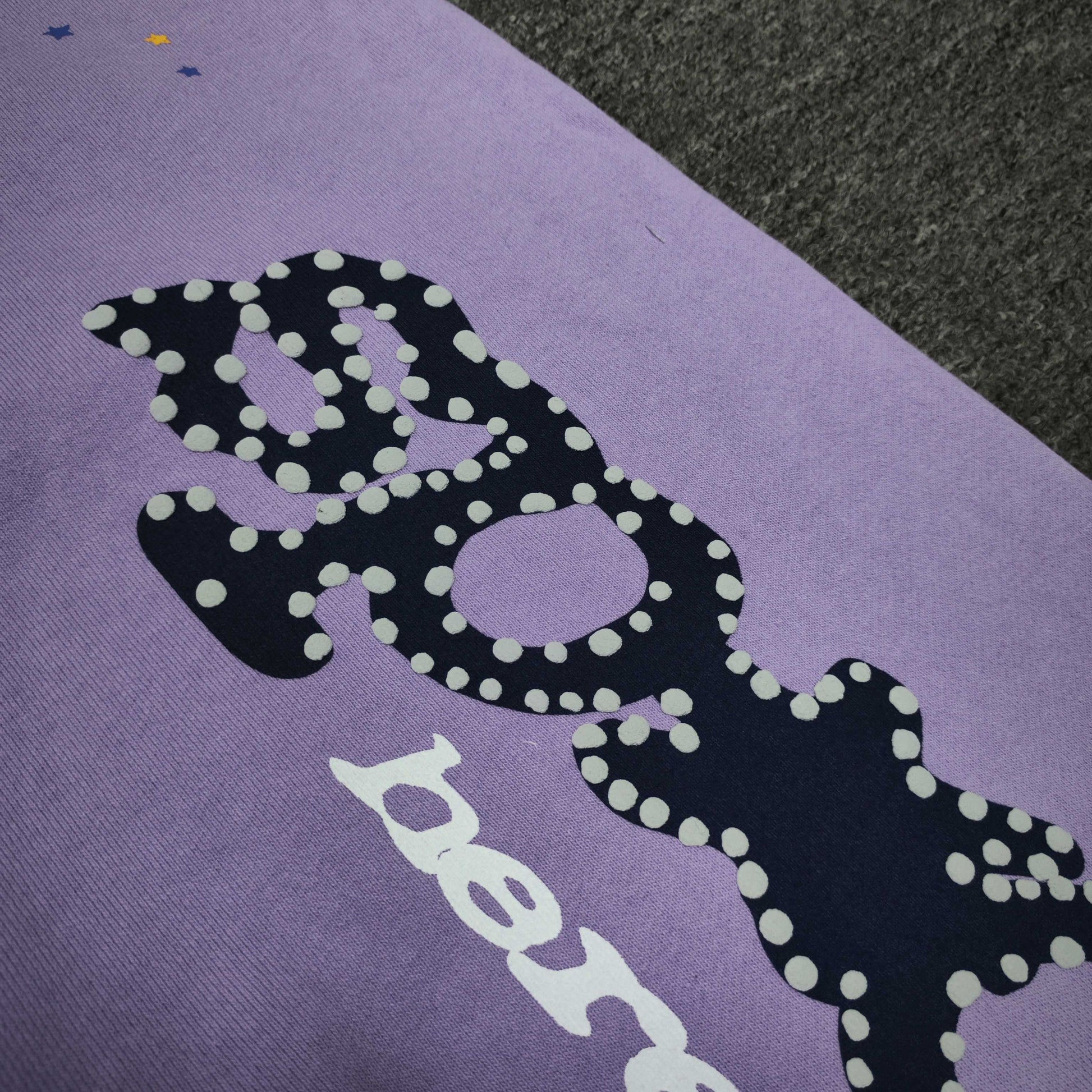 Raised navy puff-print texture on SP5DER Acai purple sweatpants
White dot detailing around the navy SP5DER graphic on Acai sweatpants
White slogan print detail on SP5DER Acai purple sweatpants