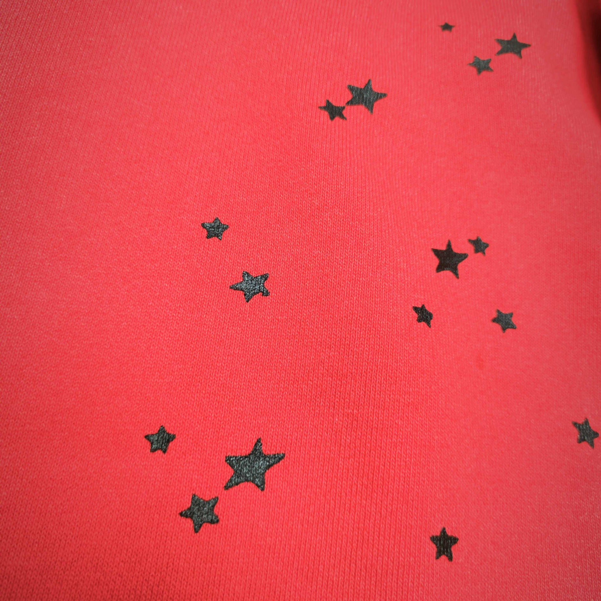 Scattered black star graphics on SP5DER P*NK V2 red sweatpants
Close-up of black star print details on red SP5DER sweatpants