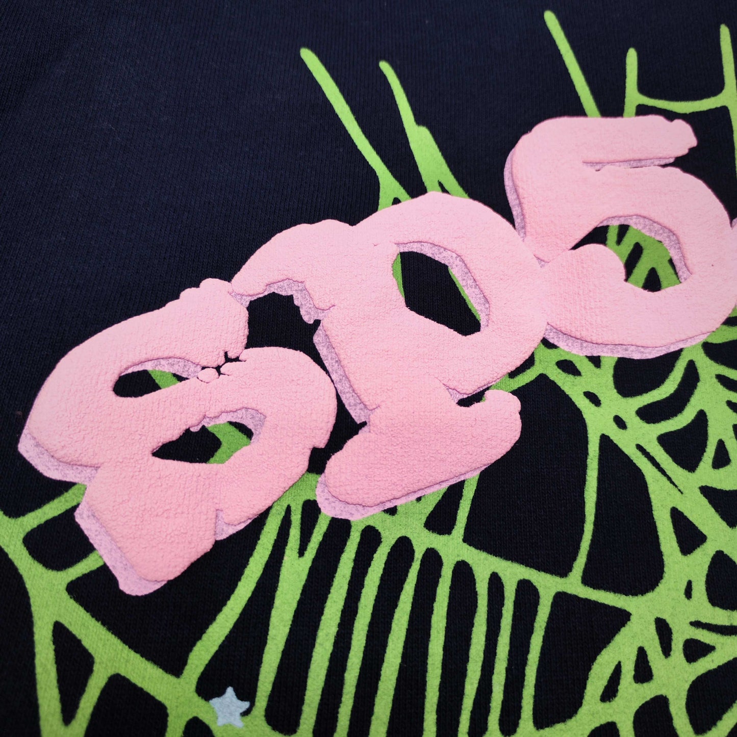 Full front artwork on Sp5der OG Web Hoodie Navy with pink puff logo, green web and stars
Close-up of raised pink SP5DER puff-print lettering on the Navy OG Web Hoodie
Side angle showing the three-dimensional pink puff-print texture on Sp5der OG Web Hoodie Navy
Close-up of mint-green spider-web artwork on Sp5der OG Web Hoodie Navy