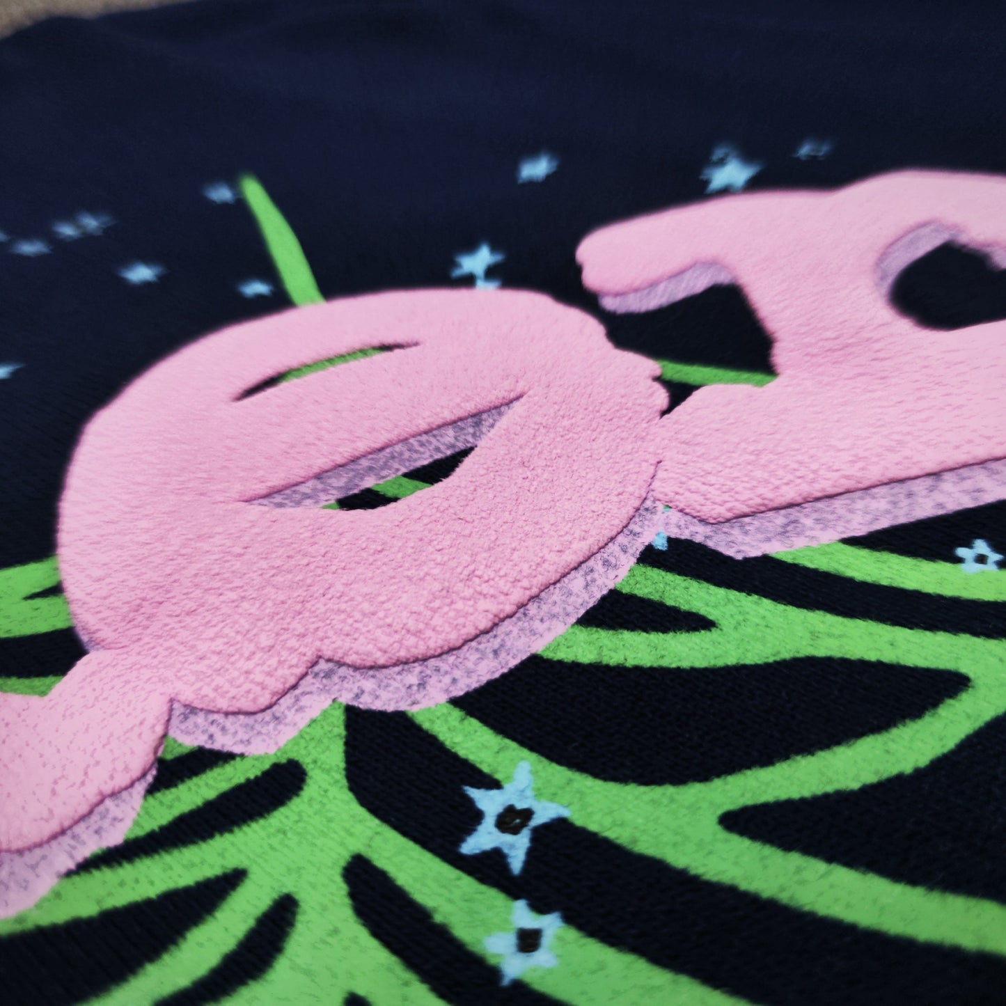 Full front artwork on Sp5der OG Web Hoodie Navy with pink puff logo, green web and stars
Close-up of raised pink SP5DER puff-print lettering on the Navy OG Web Hoodie
Side angle showing the three-dimensional pink puff-print texture on Sp5der OG Web Hoodie Navy
Close-up of mint-green spider-web artwork on Sp5der OG Web Hoodie Navy