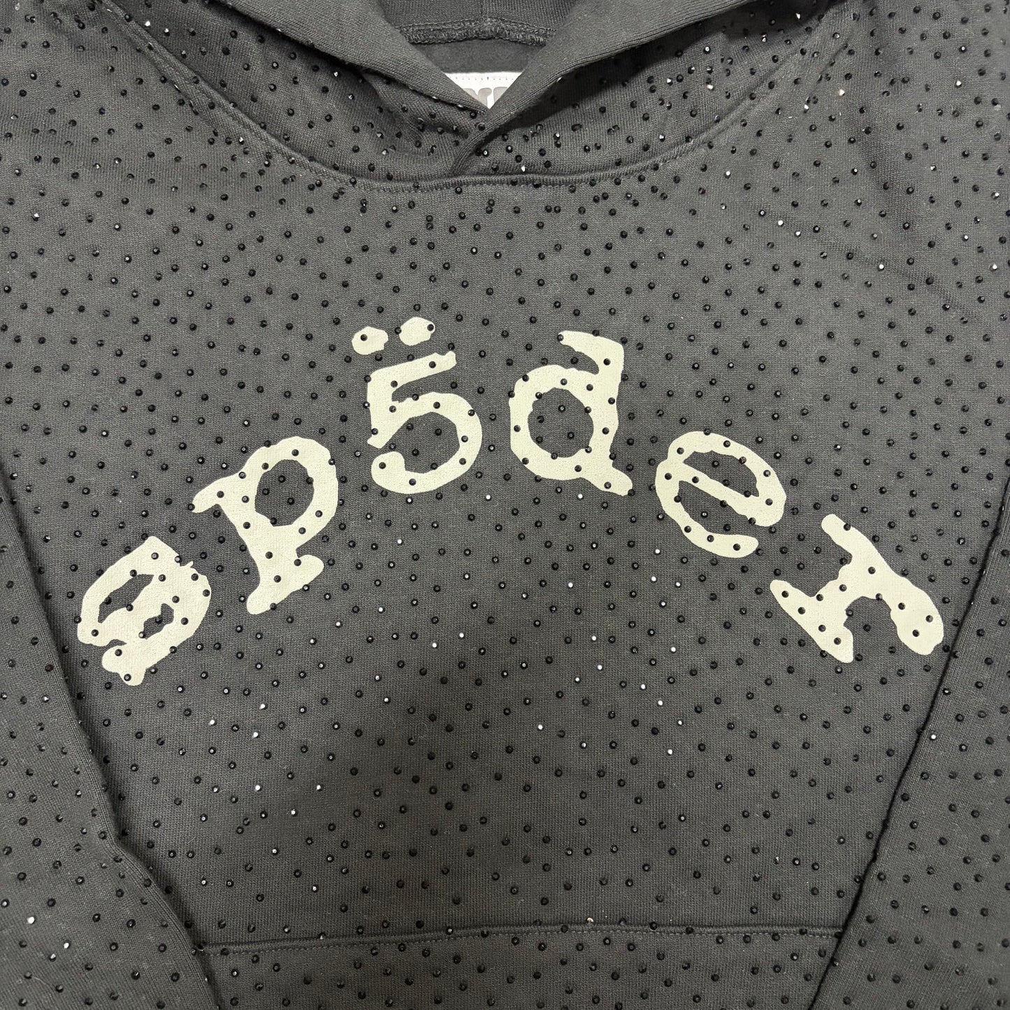 Full all-over tonal rhinestone design on Sp5der VVS Hoodie Black
Close-up of black rhinestone spacing and reflective details on Sp5der VVS Hoodie Black
Side angle showing the raised three-dimensional rhinestone texture on Sp5der VVS Hoodie
Close-up of contrasting SP5DER chest lettering on the black VVS rhinestone hoodie