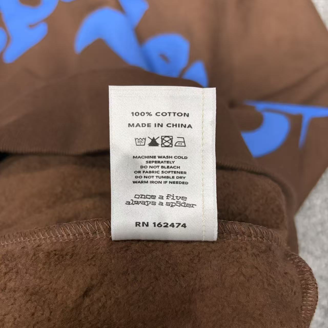 Sp5der Beluga Hoodie Brown neck label and size tag detail
Sp5der Beluga Hoodie Brown care label and washing instruction detail