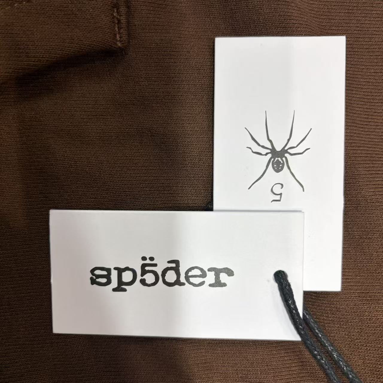 Sp5der Beluga Hoodie Brown neck label and size tag detail
Sp5der Beluga Hoodie Brown care label and washing instruction detail