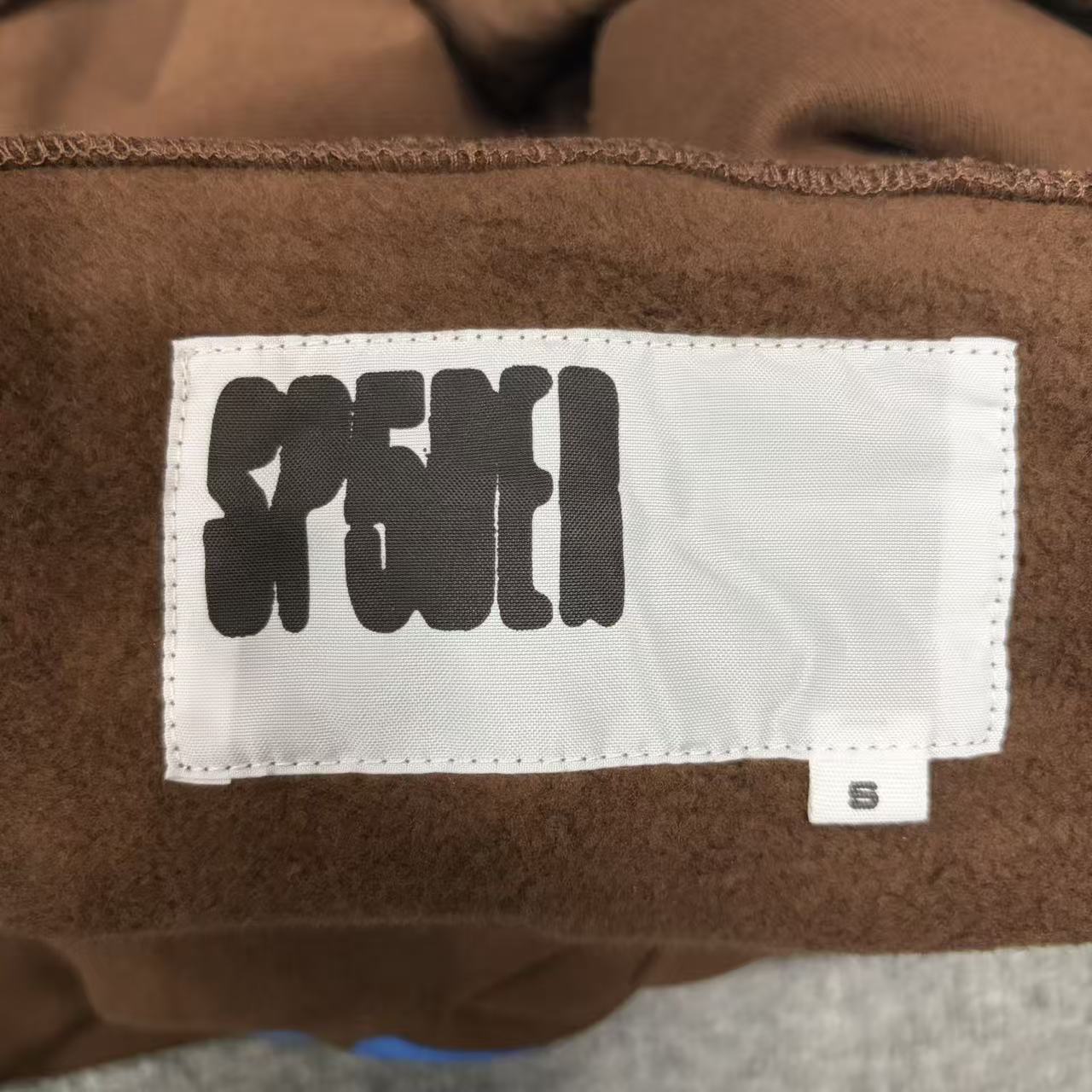 Sp5der Beluga Hoodie Brown neck label and size tag detail
Sp5der Beluga Hoodie Brown care label and washing instruction detail