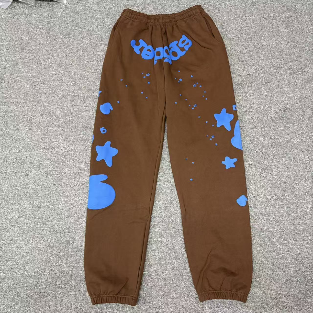 SP5DER Beluga V2 brown sweatpants front view with blue logo and oversized star graphics