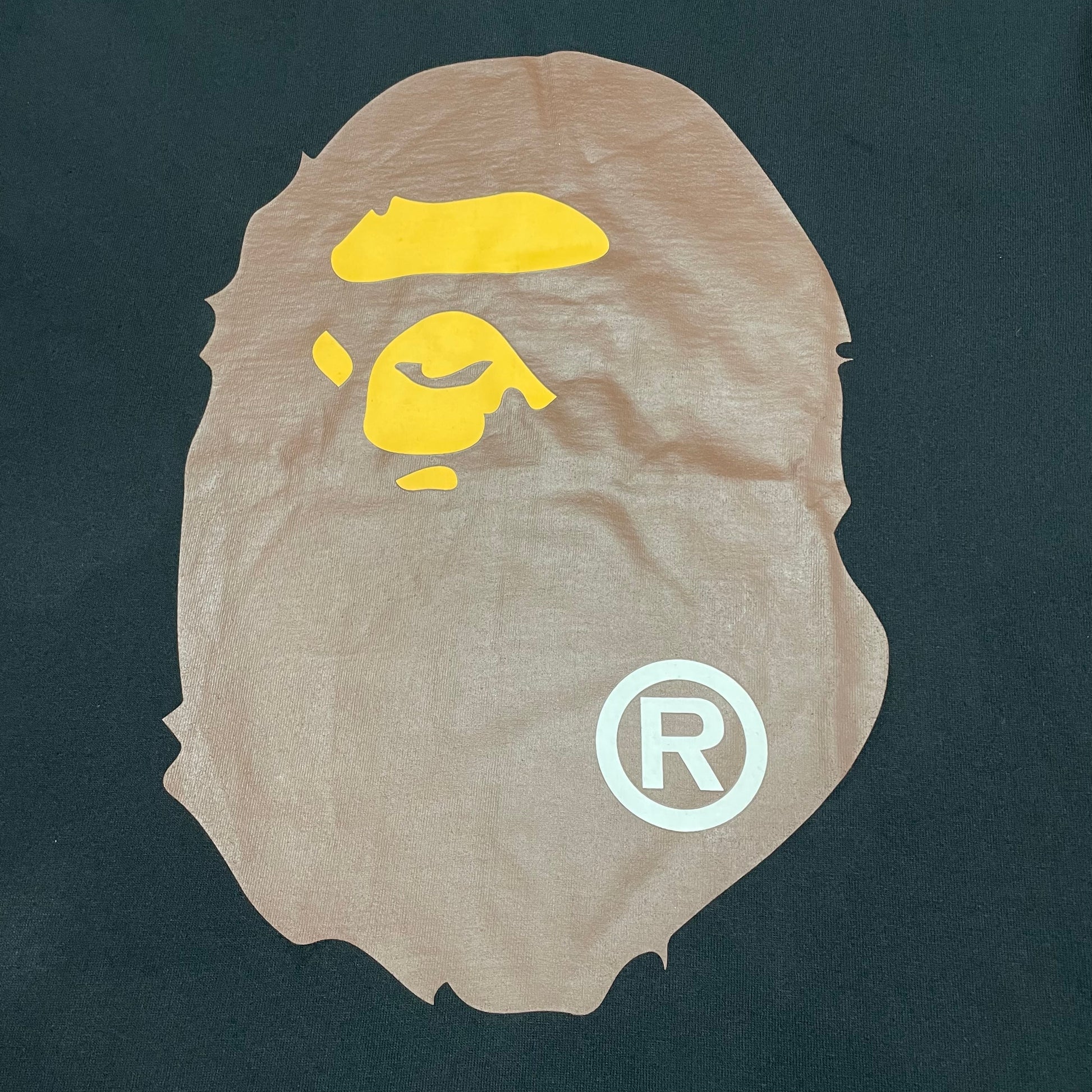 Close-up of brown and yellow Ape Head graphic on black BAPE T-shirt