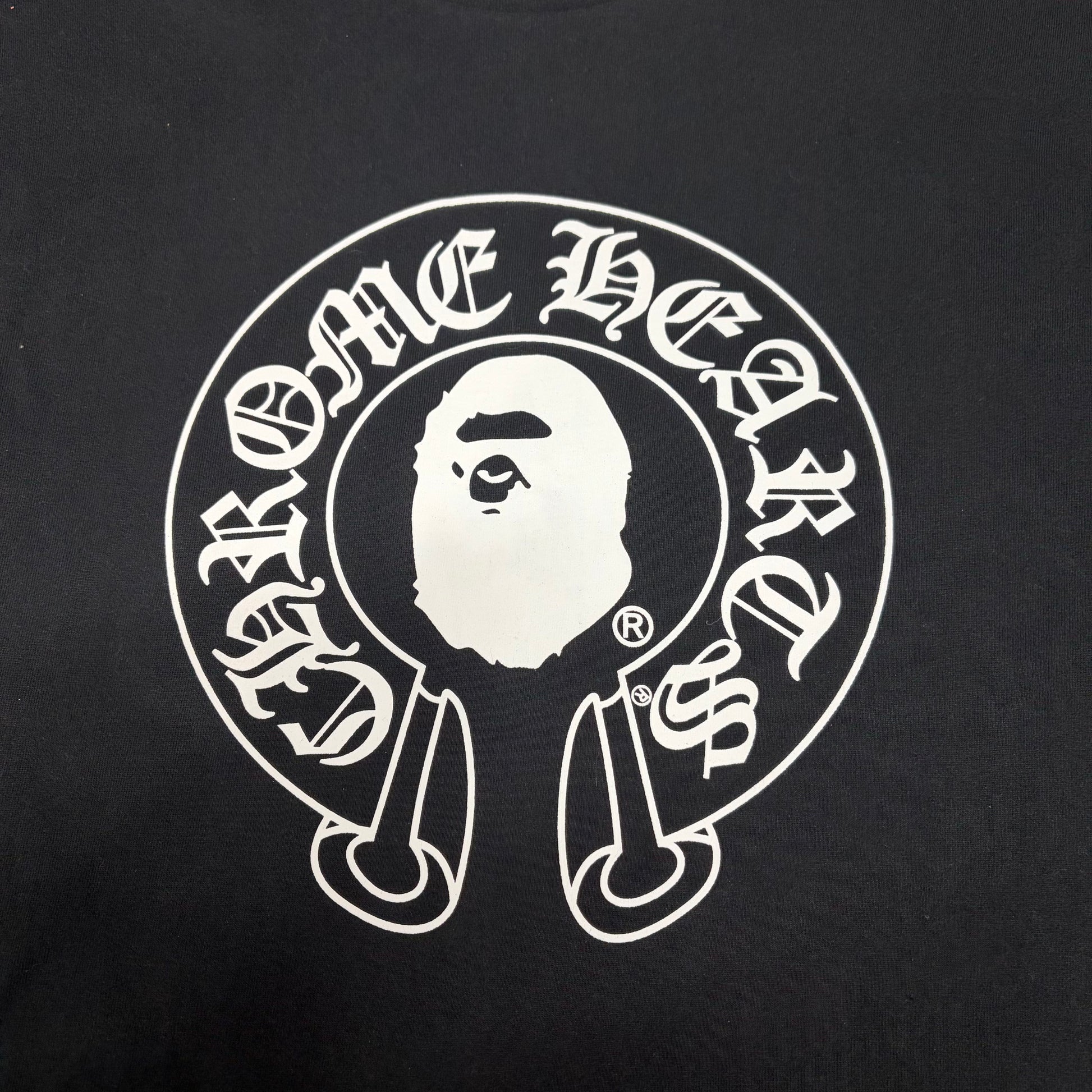 White Chrome Hearts horseshoe and Ape Head graphic on black BAPE T-shirt
Close-up of white BAPE x Chrome Hearts front graphic on black T-shirt
Gothic Chrome Hearts lettering detail on black BAPE collaboration T-shirt
Close-up of white Ape Head logo on black BAPE x Chrome Hearts T-shirt