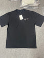 Black crew‑neck short‑sleeve tee flat lay, small distressed logo graphic on left chest, paper brand hangtag attached