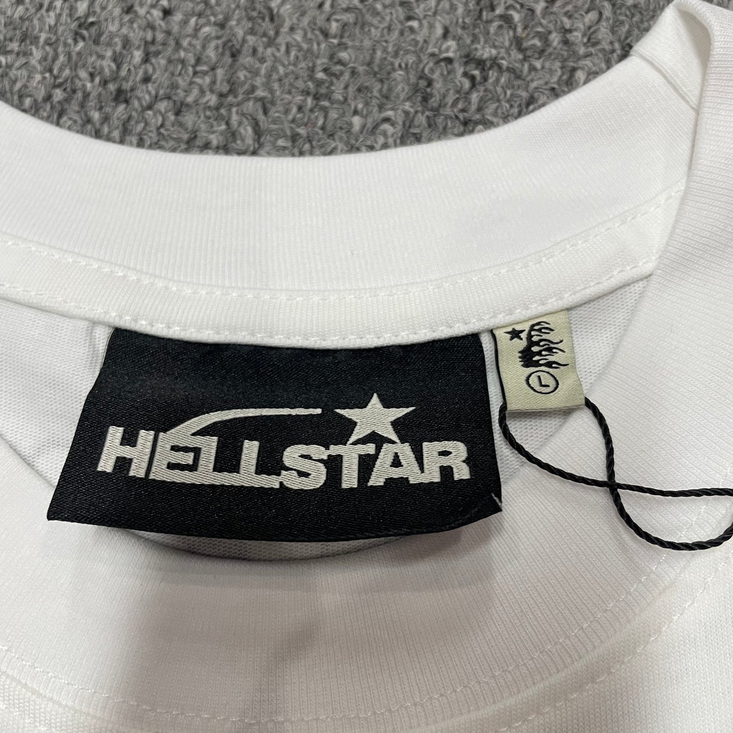 Hellstar branded neck label and crew-neck stitching on the Path to Paradise T-Shirt
Close-up of the Hellstar flame logo hangtag and attachment details