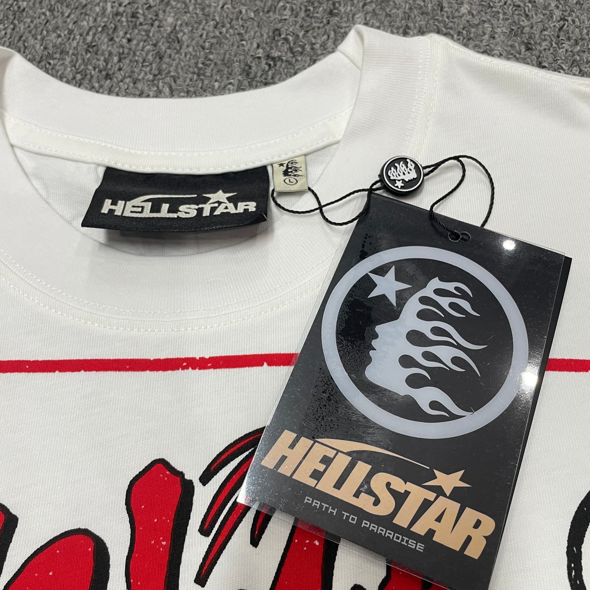 Hellstar branded neck label and crew-neck stitching on the Path to Paradise T-Shirt
Close-up of the Hellstar flame logo hangtag and attachment details